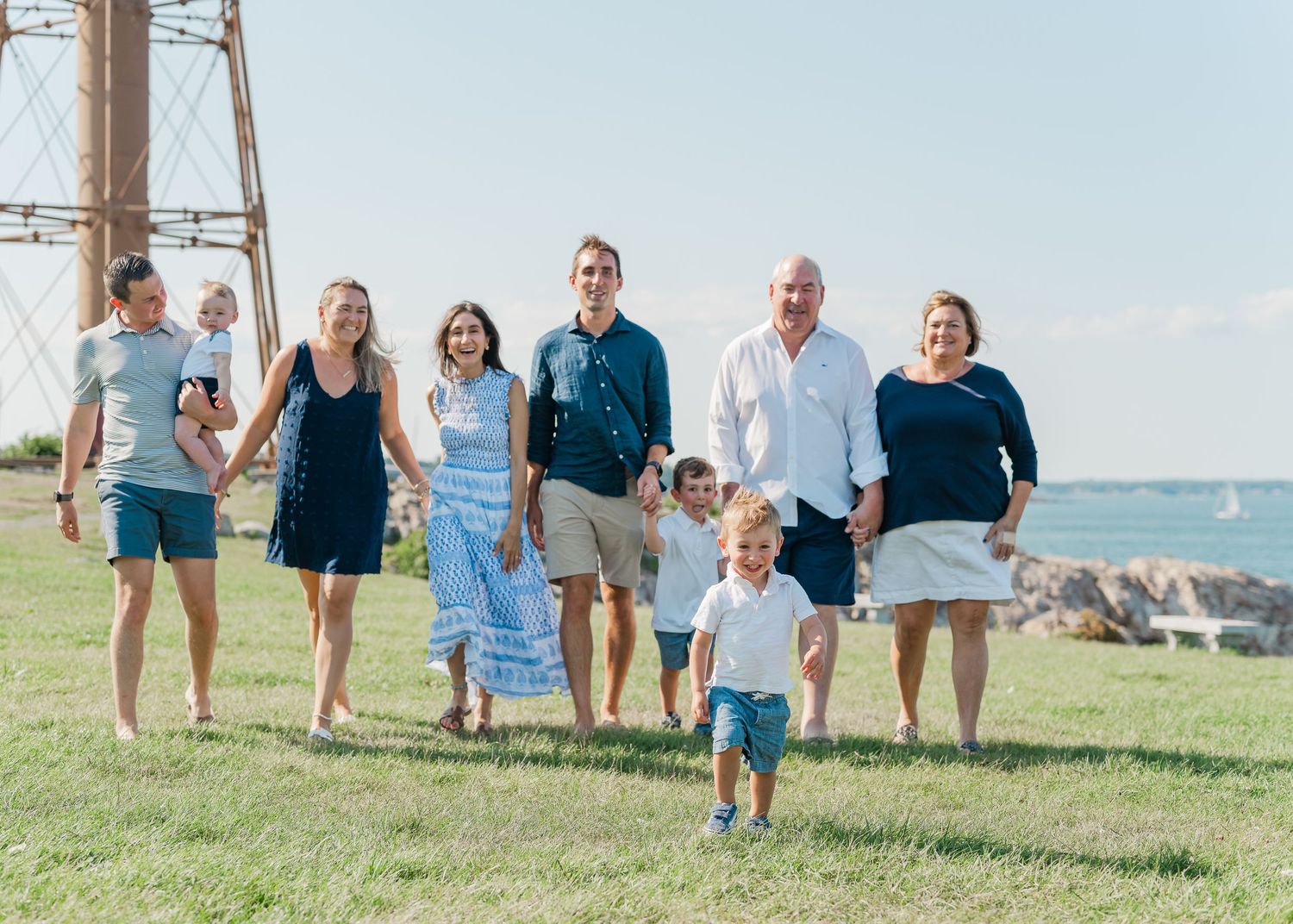 A happy family walks together on a grassy hillside by the ocean on a bright sunny day.