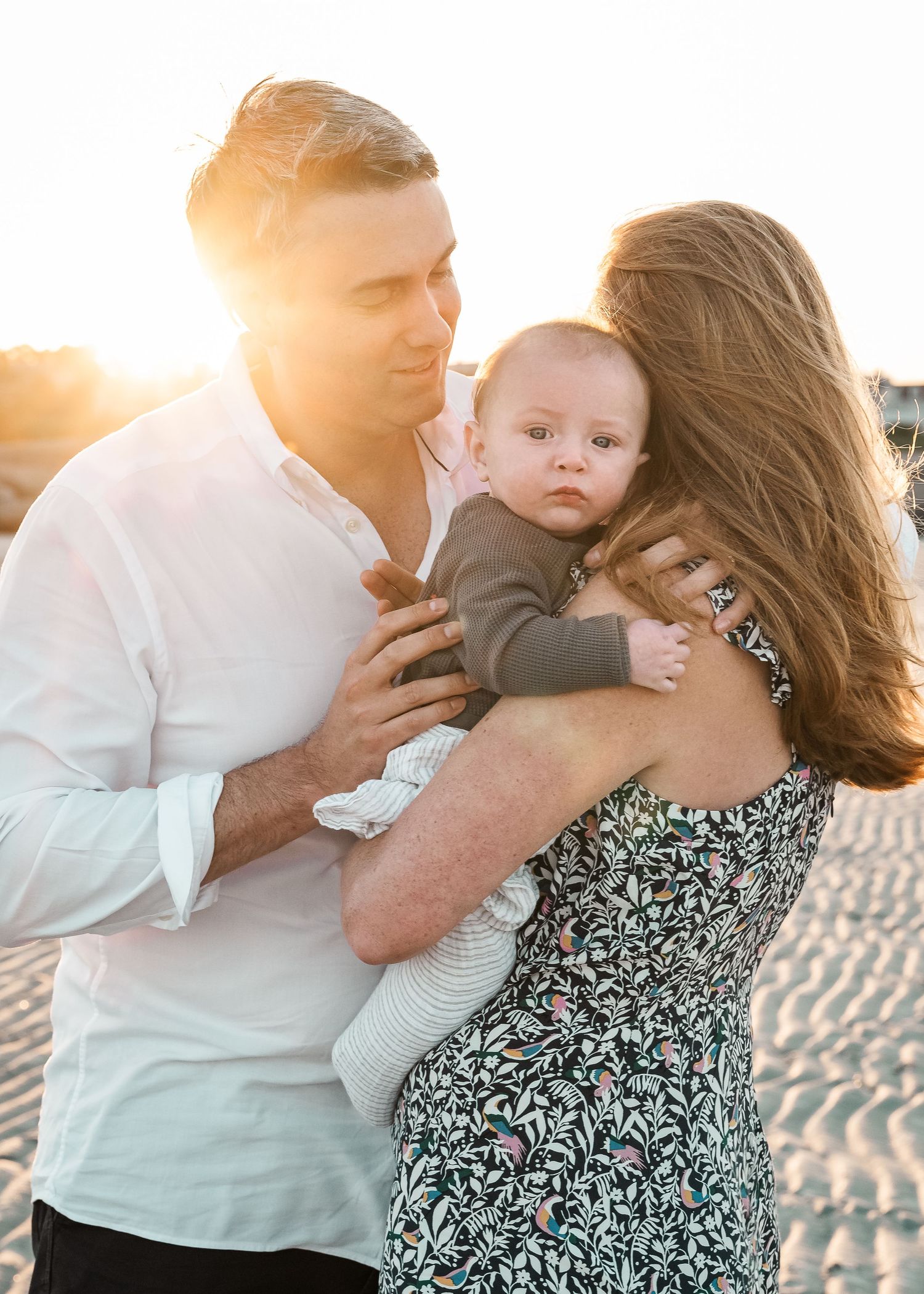 A family embraces on the beach at sunset with warm golden light behind them.