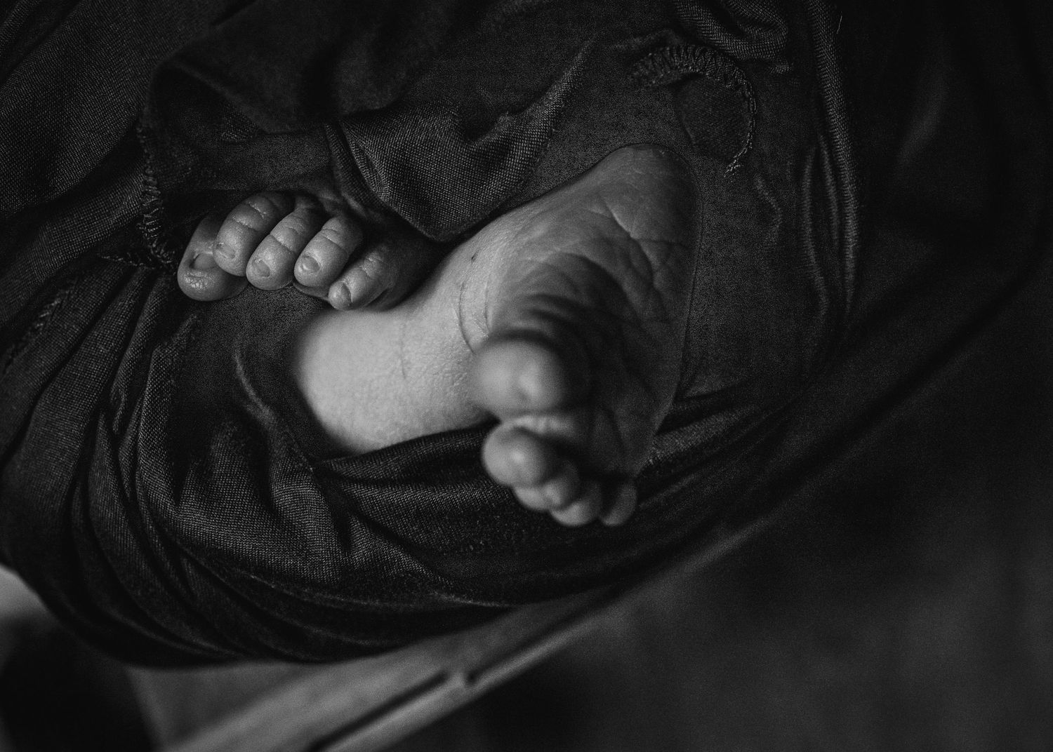 Black and white image of tiny newborn feet wrapped in dark fabric.