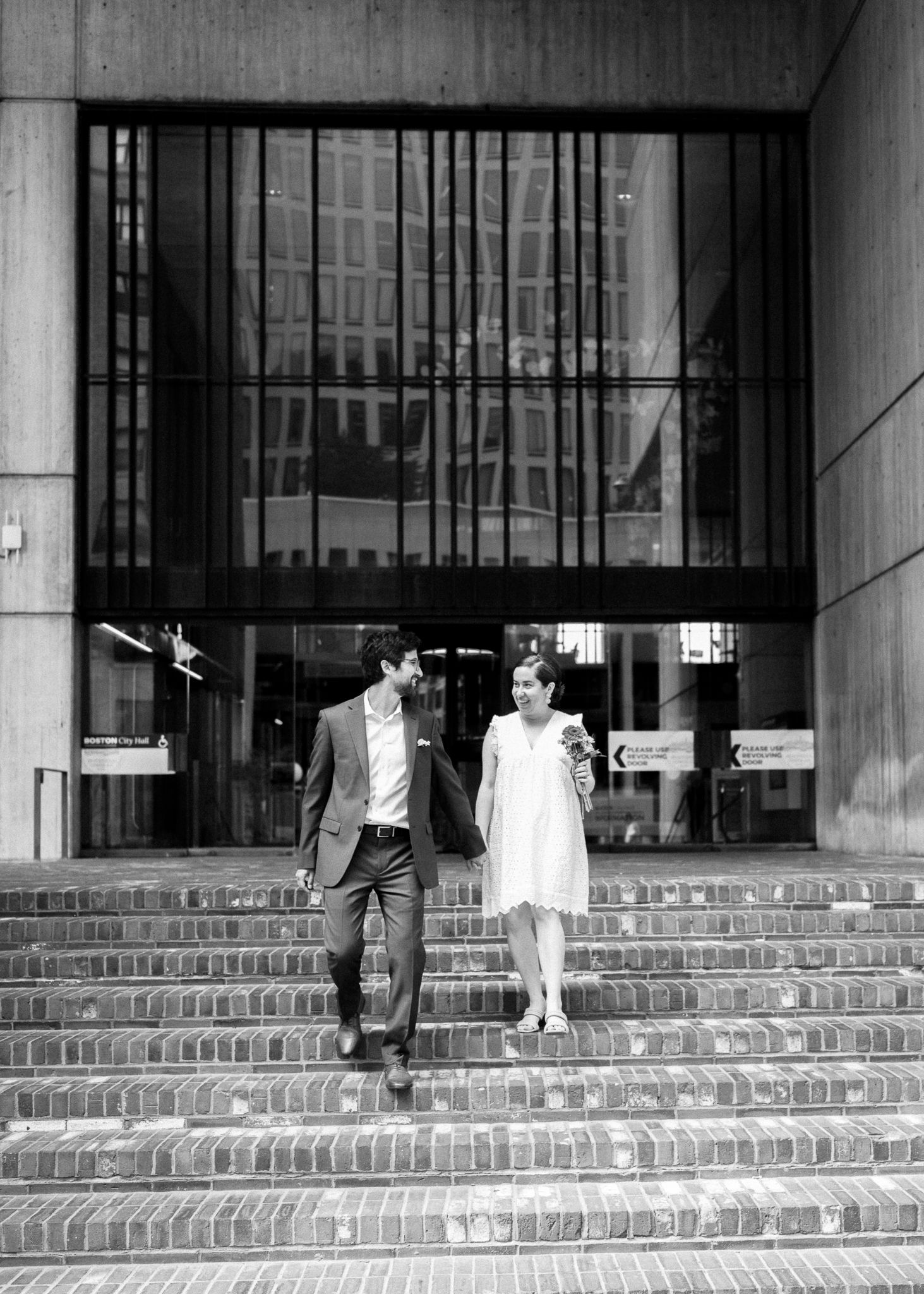 A black and white photo of a couple descending concrete steps outside a modern building.