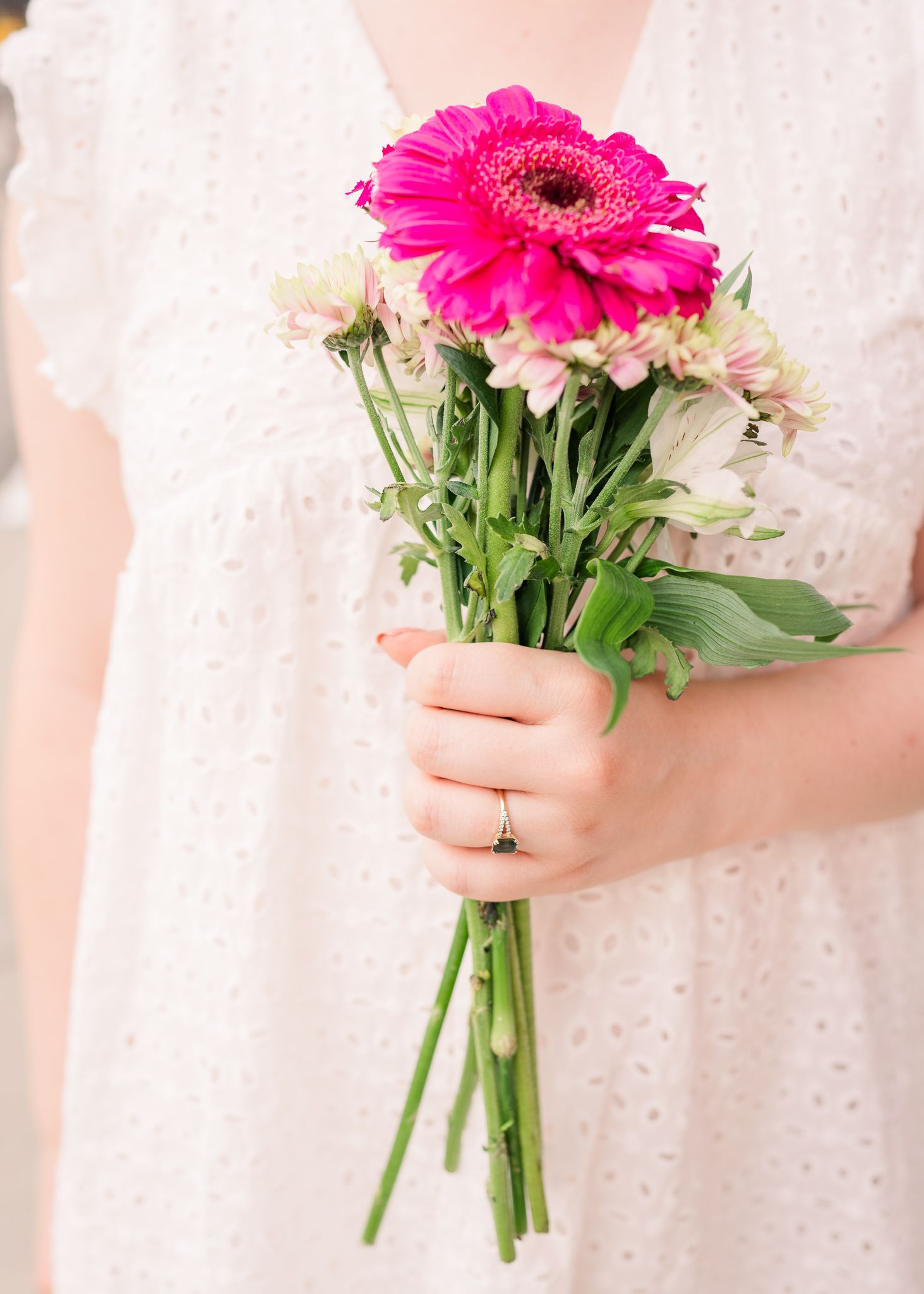 A vibrant pink gerbera daisy mixed with white flowers in a delicate bridal bouquet held against a lace dress.