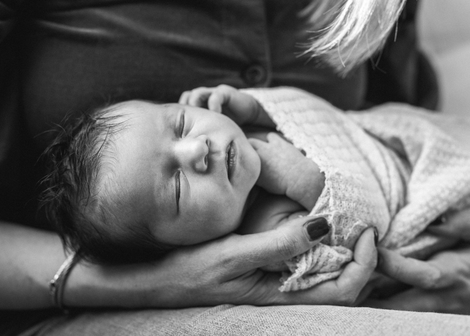 Black and white image of sleeping newborn wrapped in soft blanket.