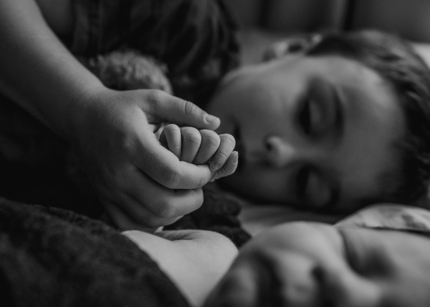 Black and white close up of hand holding tiny baby foot in intimate moment.