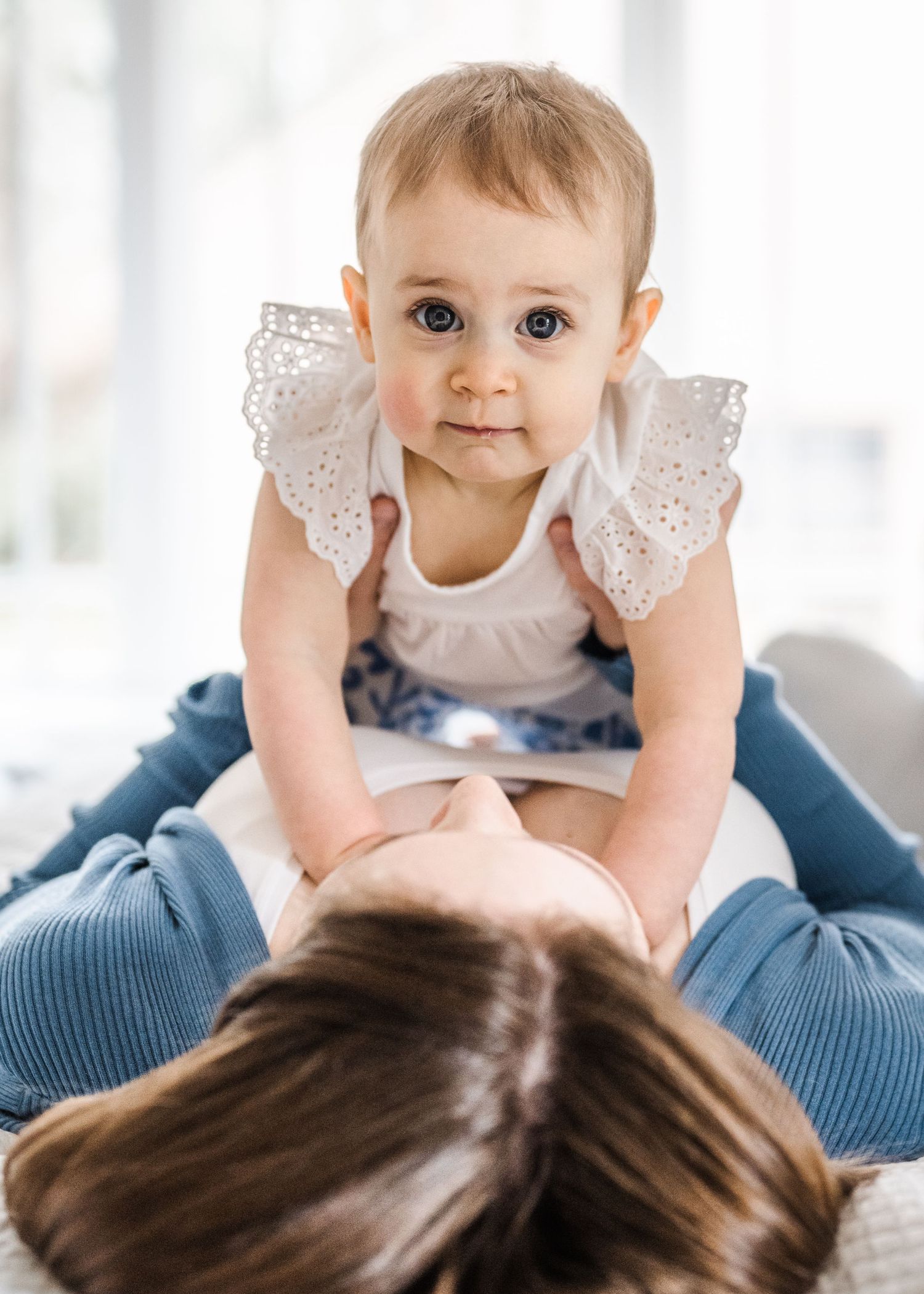 A baby wearing a white lace dress leaning forward on a blue surface.
