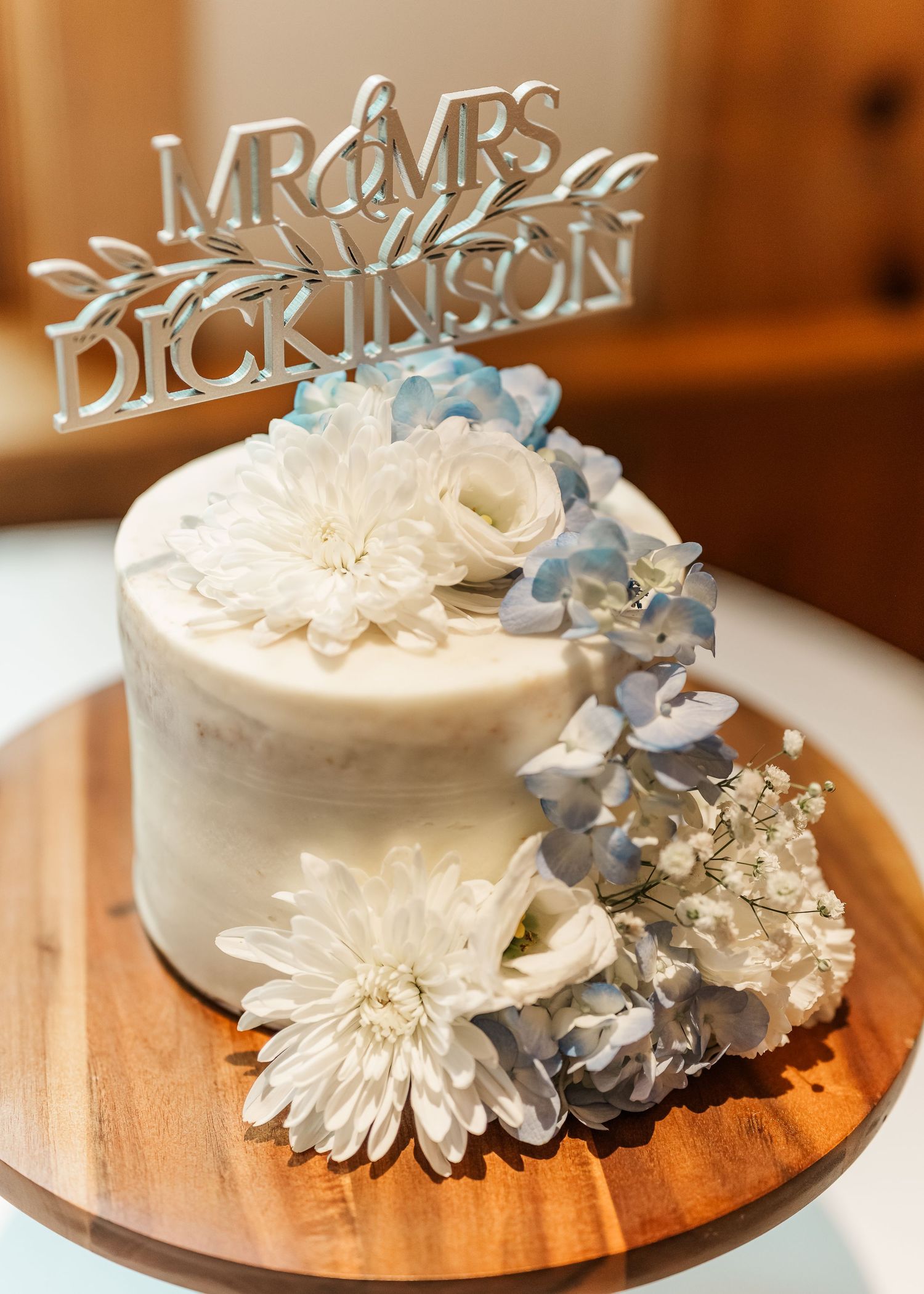 Close-up view of elegant white wedding cakes adorned with delicate blue and white sugar flowers arranged on wooden platforms.