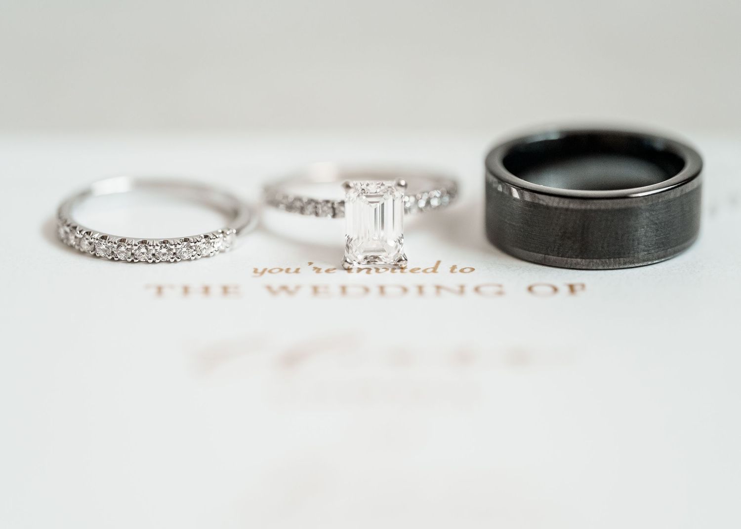 Three wedding rings laid out on white surface showing silver diamonds bands and black tungsten band details.