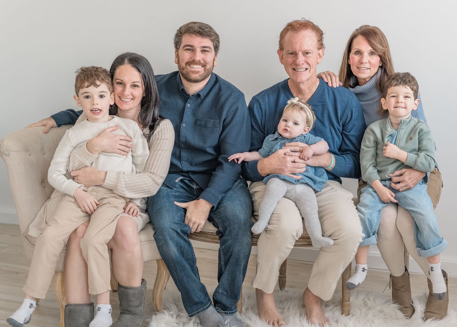 A family sitting together on a light gray couch wearing coordinated casual outfits in neutral tones.