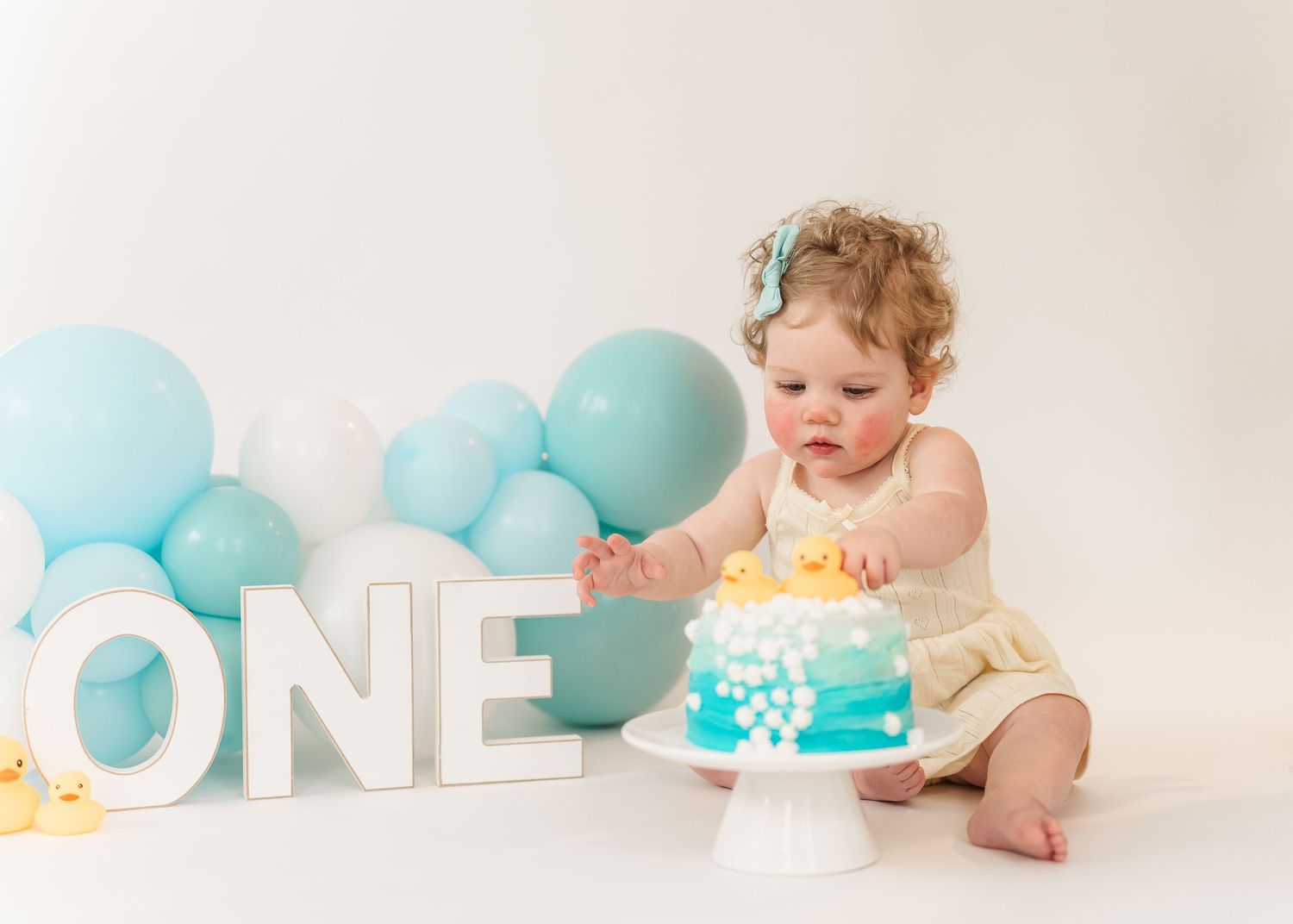 Cake smash. Baby in diaper crawls near pastel blue balloons and white ONE letters for first birthday photoshoot.