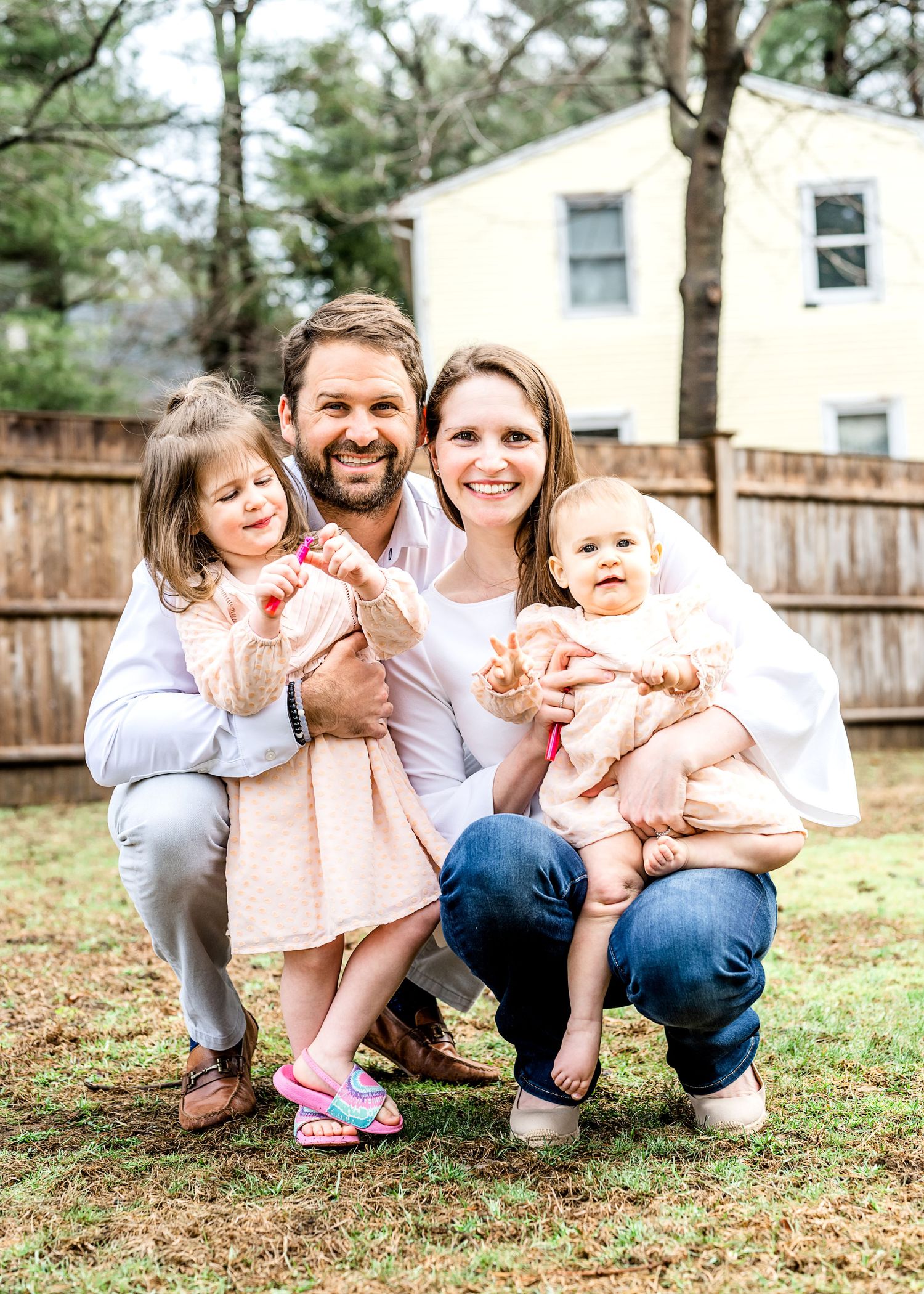 A joyful family photo taken outdoors in front of a house with a wooden fence.