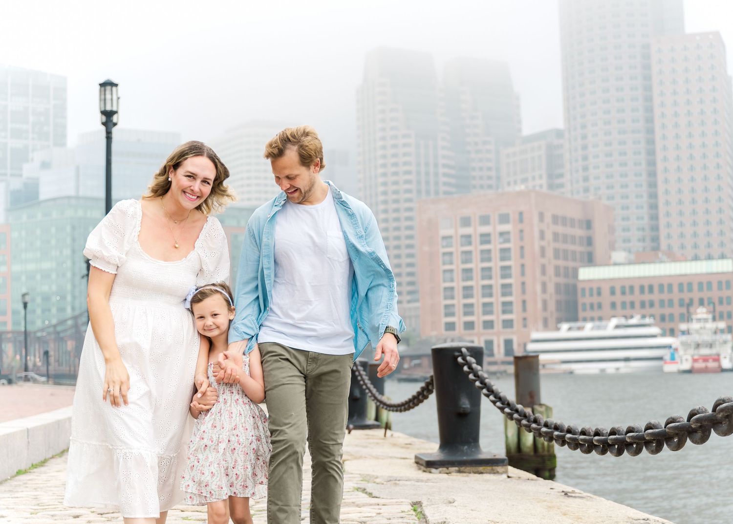 Family standing together on foggy waterfront with city skyline in background.