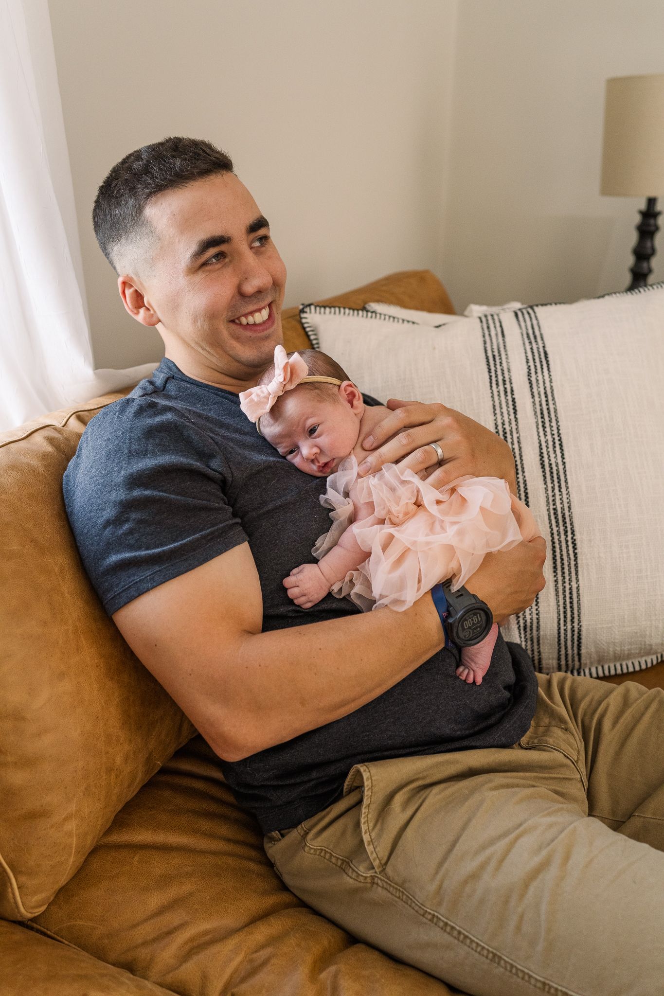 Tender moment of father and baby relaxing together on tan leather couch.