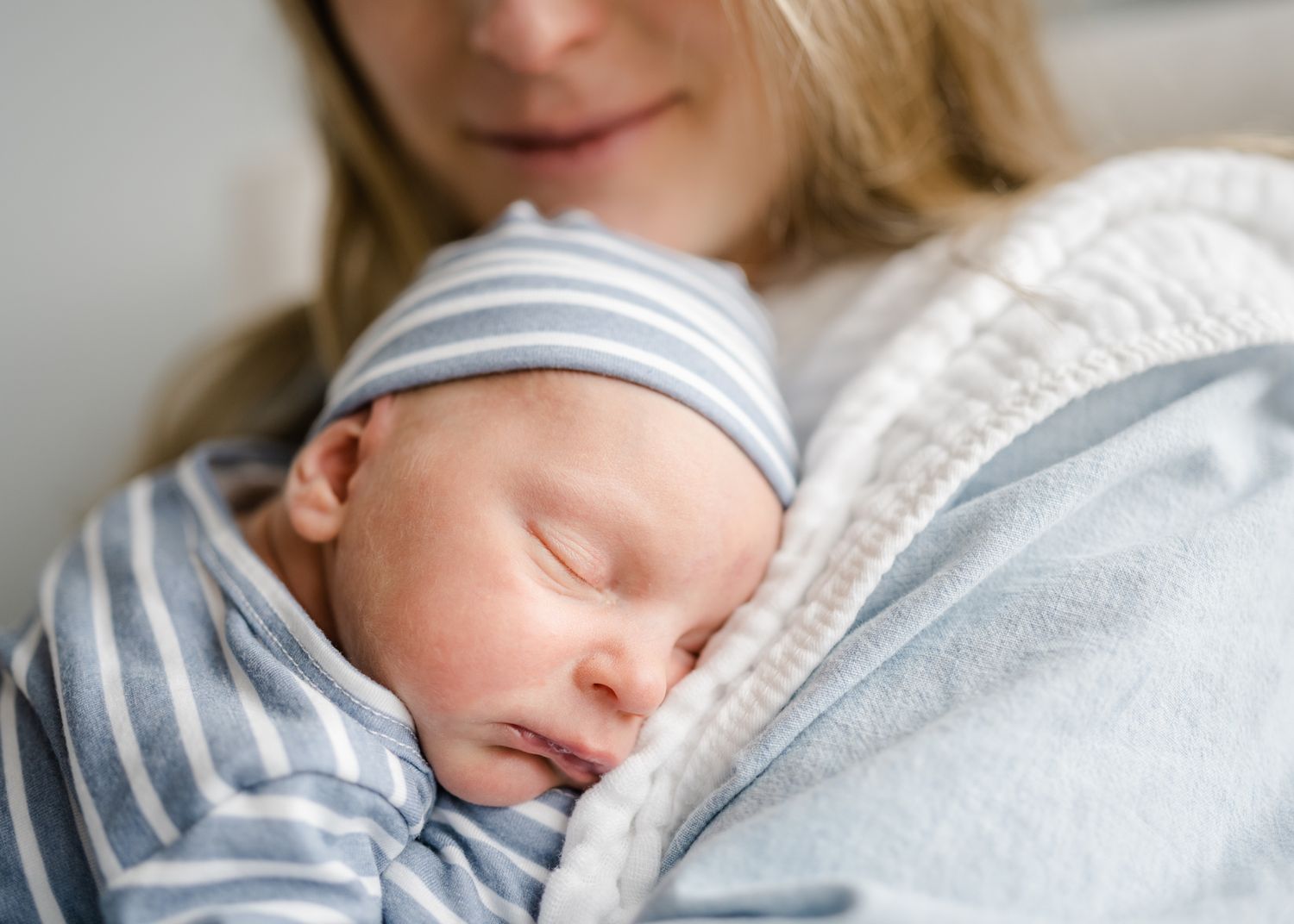 Peaceful sleeping newborn in striped outfit snuggled close in knit sweater.