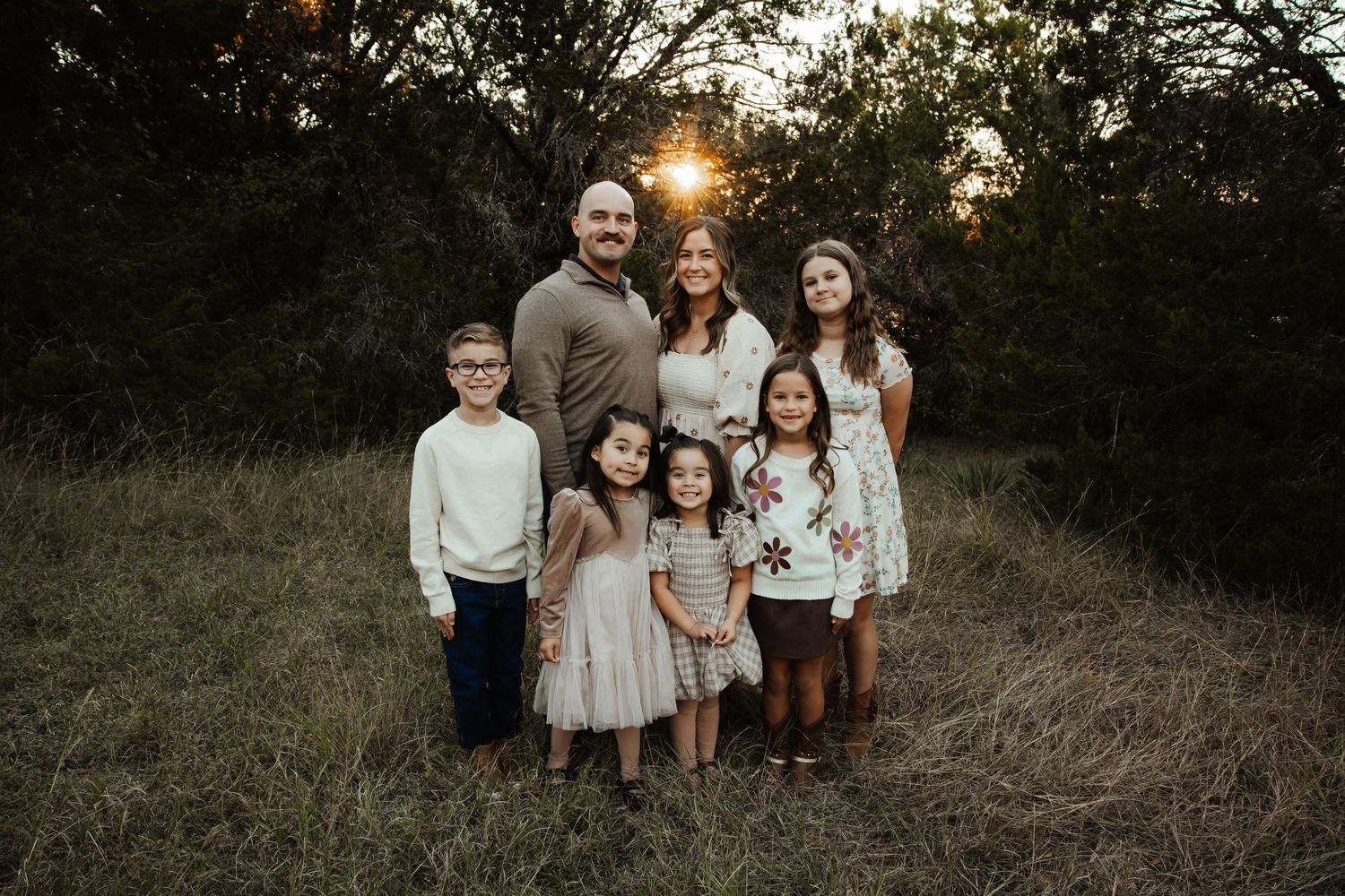 Family of seven posing together in a grassy field at golden hour sunset.