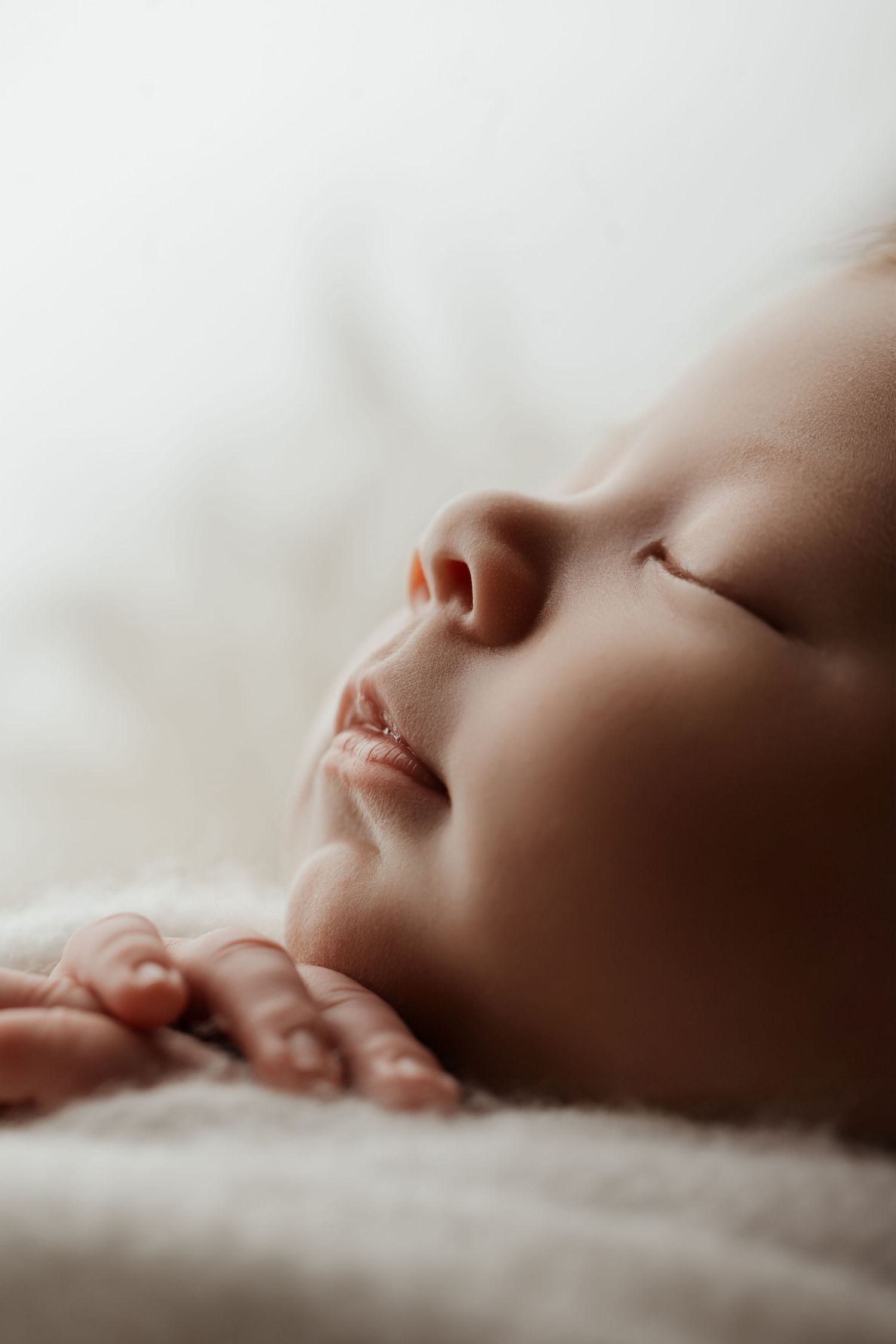 Close-up of a peaceful sleeping newborn baby with tiny hands resting on a soft white blanket.