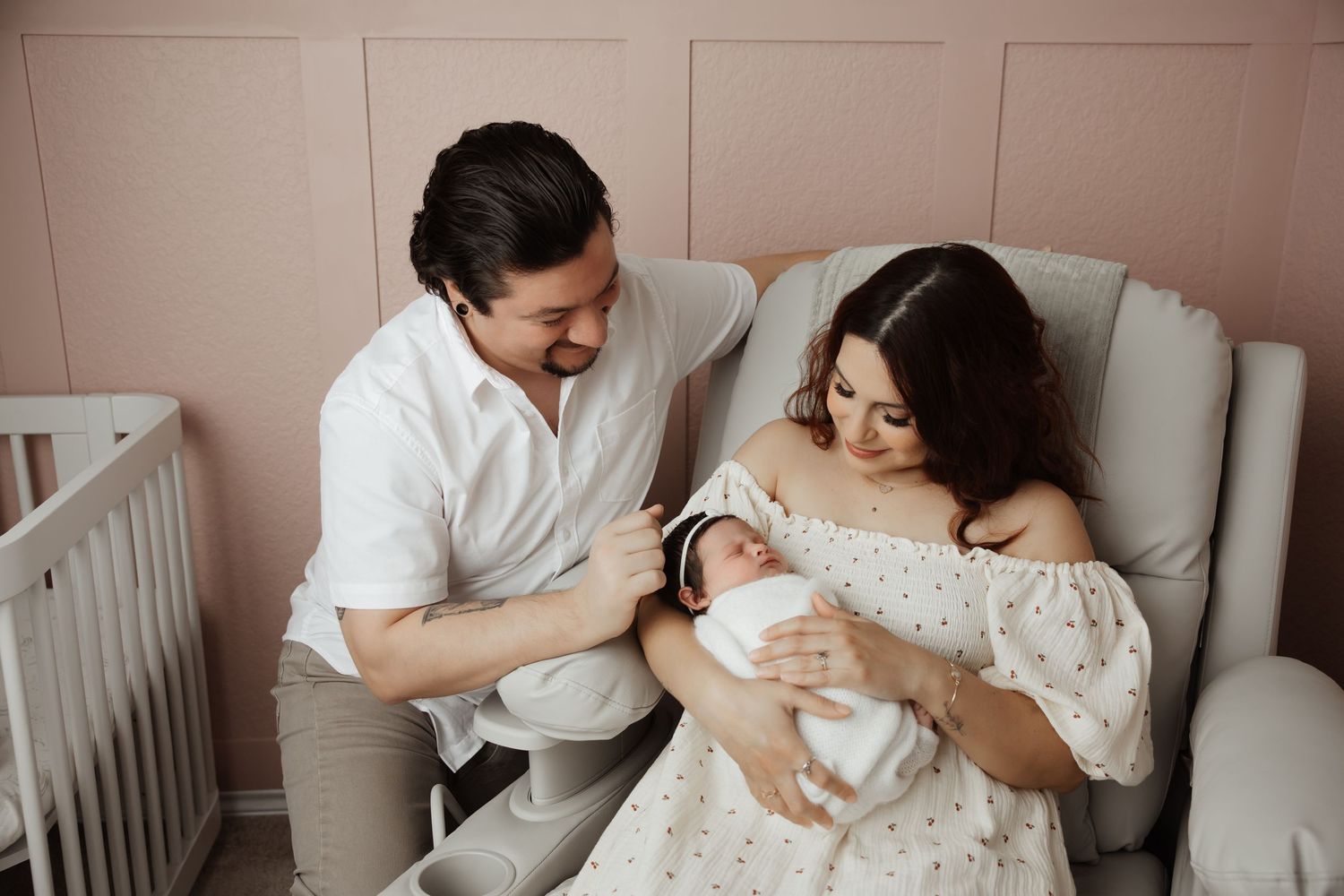 Happy new parents in pink nursery smiling at their swaddled newborn baby girl together.