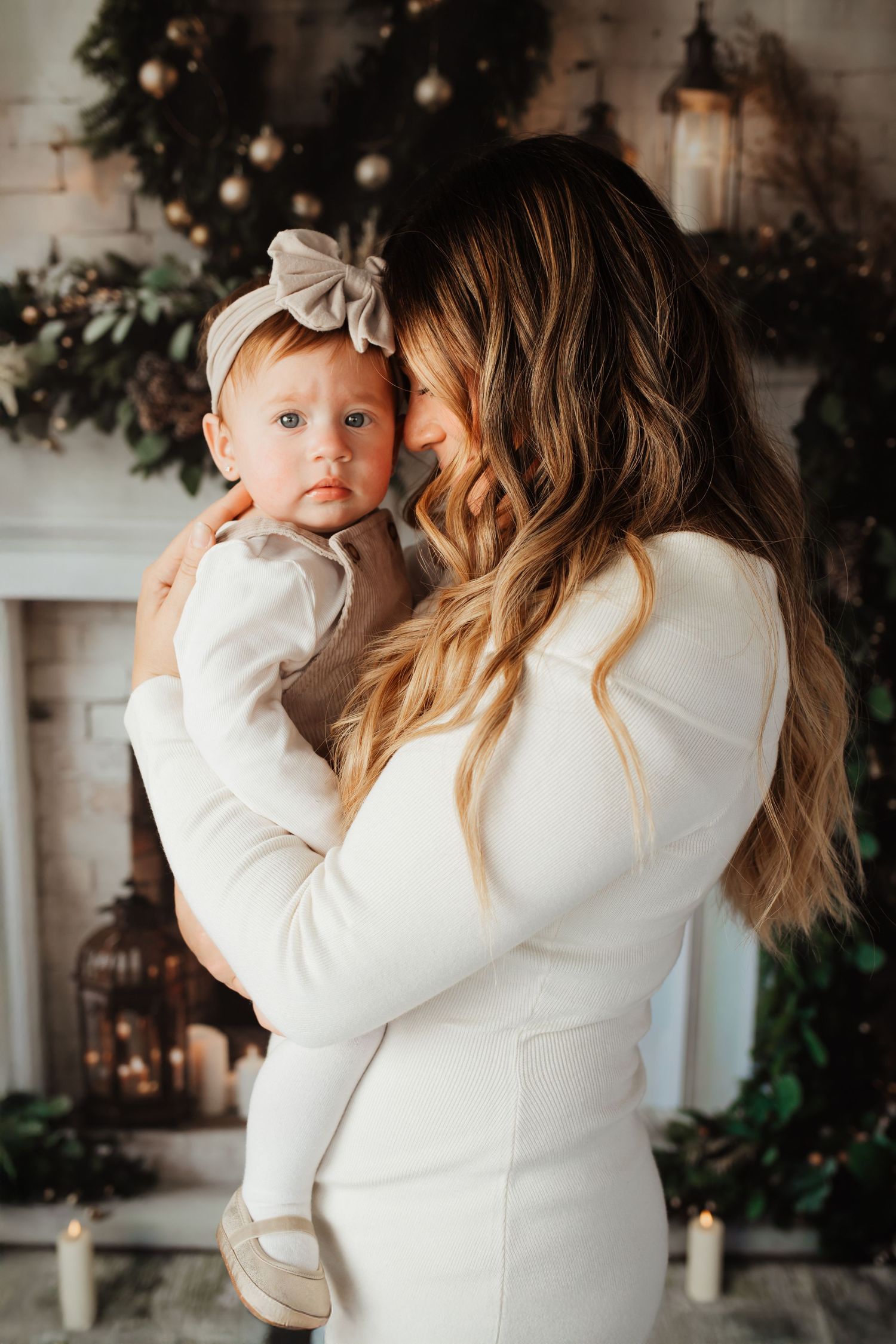 Mother in white dress tenderly holding her baby girl near Christmas decor.