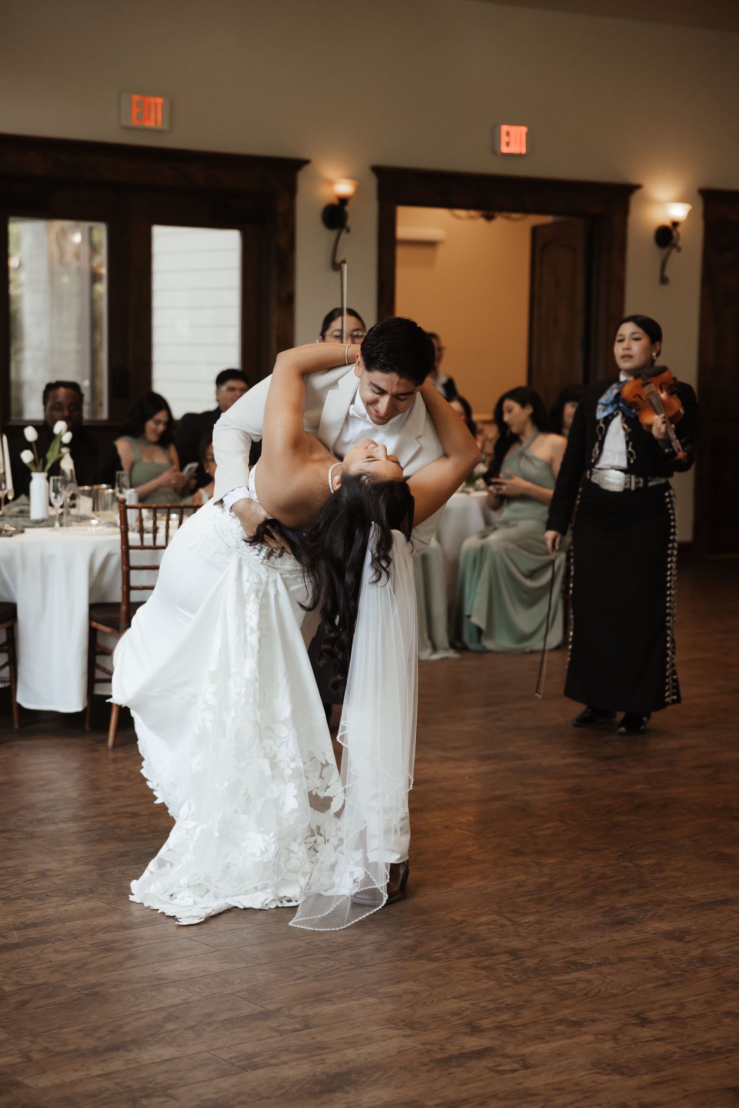 Bride and groom share a romantic dip dance at their wedding reception while a mariachi violinist performs.