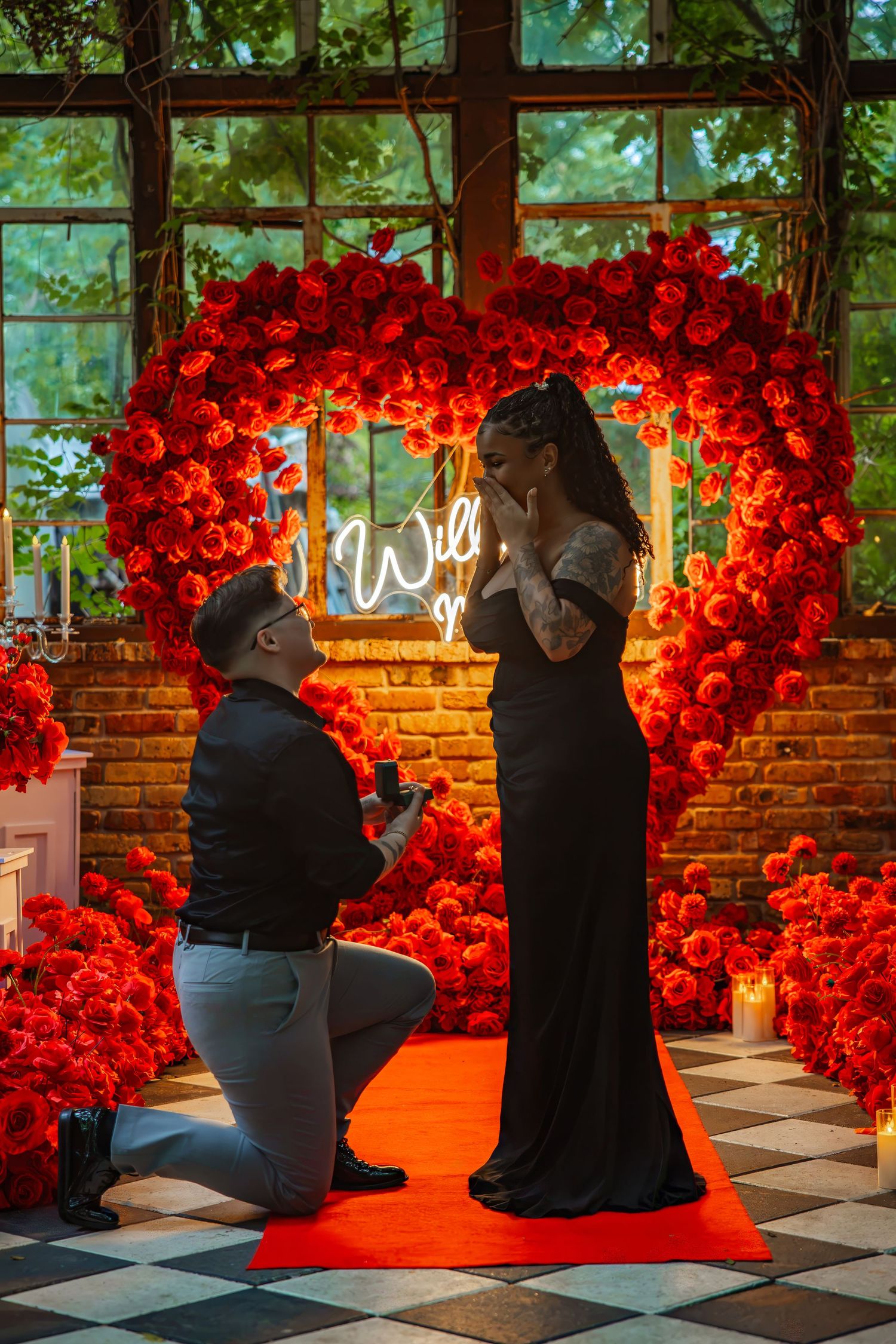 Man proposes on one knee amid red roses heart arch with neon sign, woman in black dress reacts emotionally.
