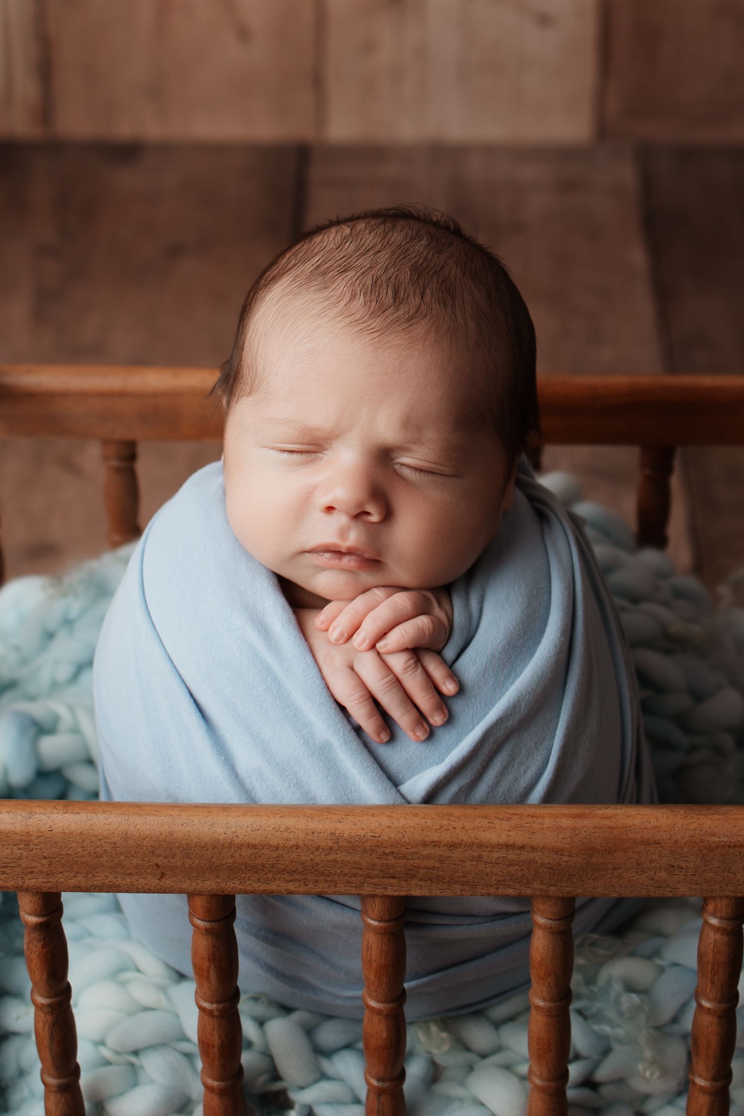Serene newborn baby wrapped in a soft blue swaddle resting in a miniature wooden crib.