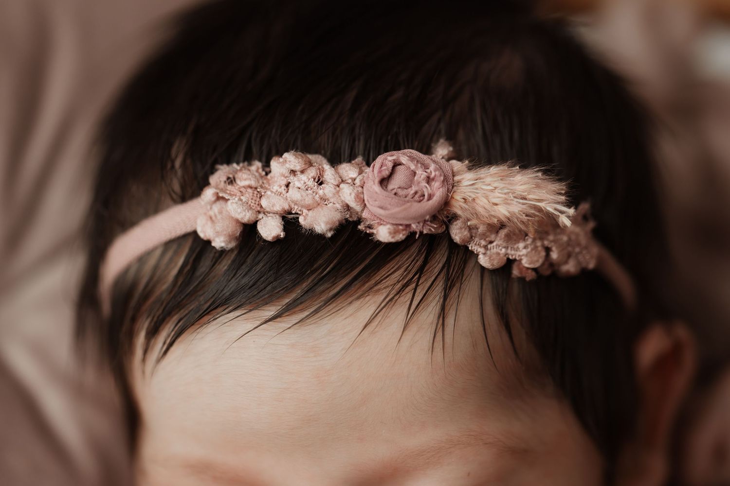 Close-up of a delicate pink floral lace headband on a newborn baby girls dark hair.