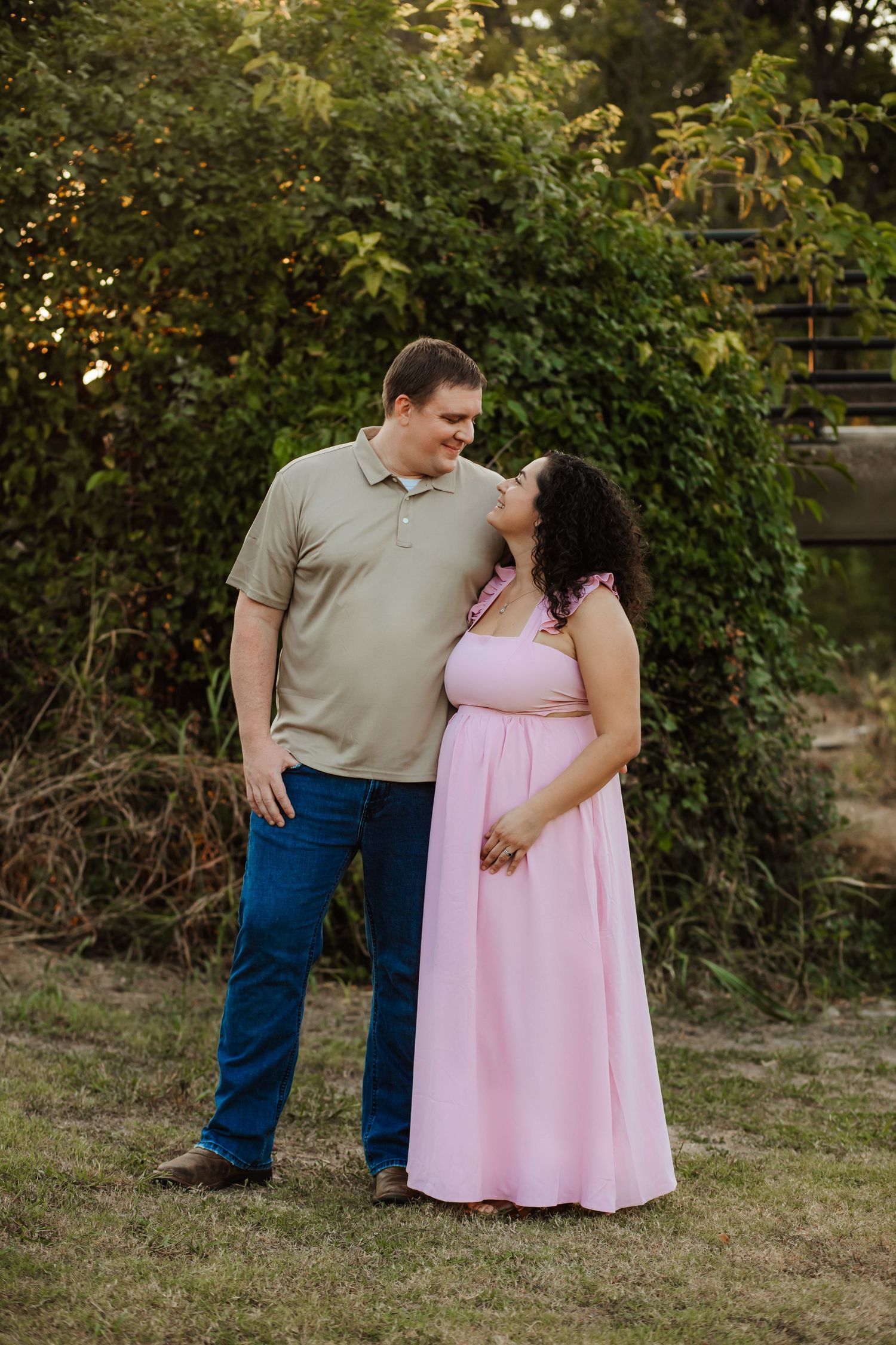 A couple shares a romantic glance while standing together in a lush garden during an outdoor portrait session.