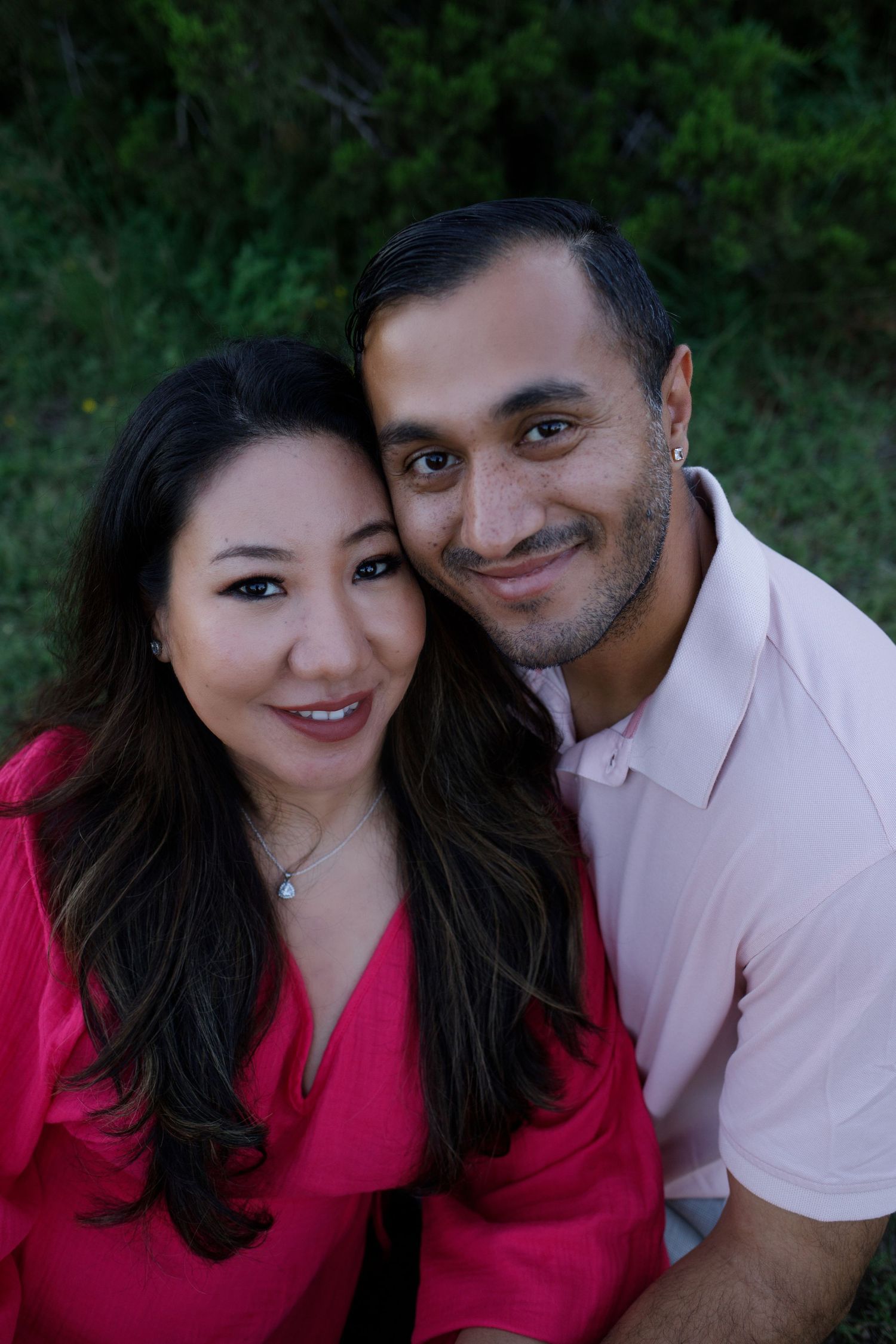 Smiling couple in pink outfits posing closely together outdoors for portrait photography.
