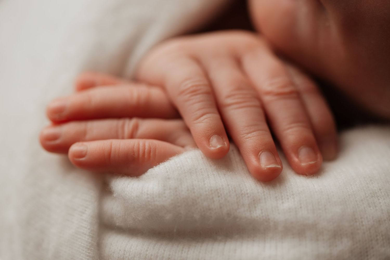 Close-up of delicate newborn baby hands resting gently on a soft white blanket.