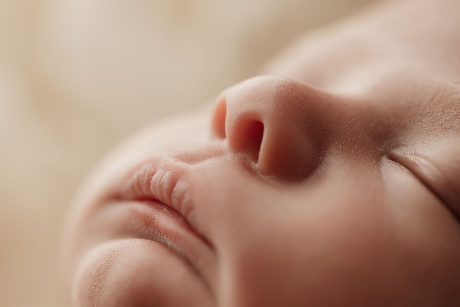 Extreme close-up of a sleeping newborn babys nose and lips on a soft blanket.