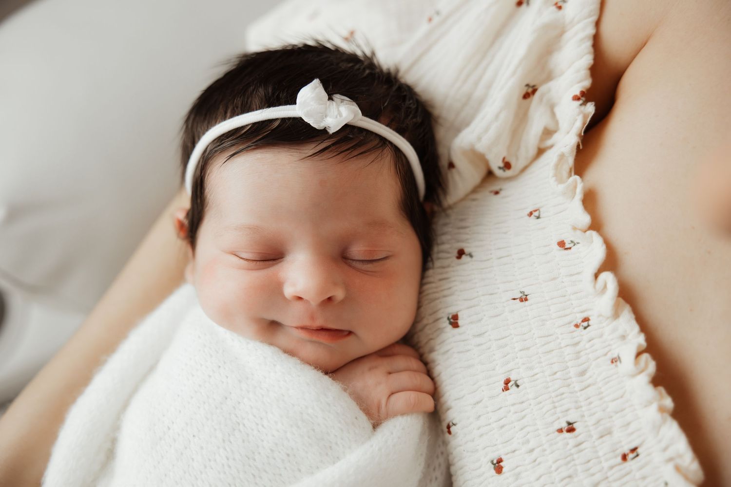 Sleeping newborn baby girl in white swaddle with bow headband during lifestyle newborn photography.