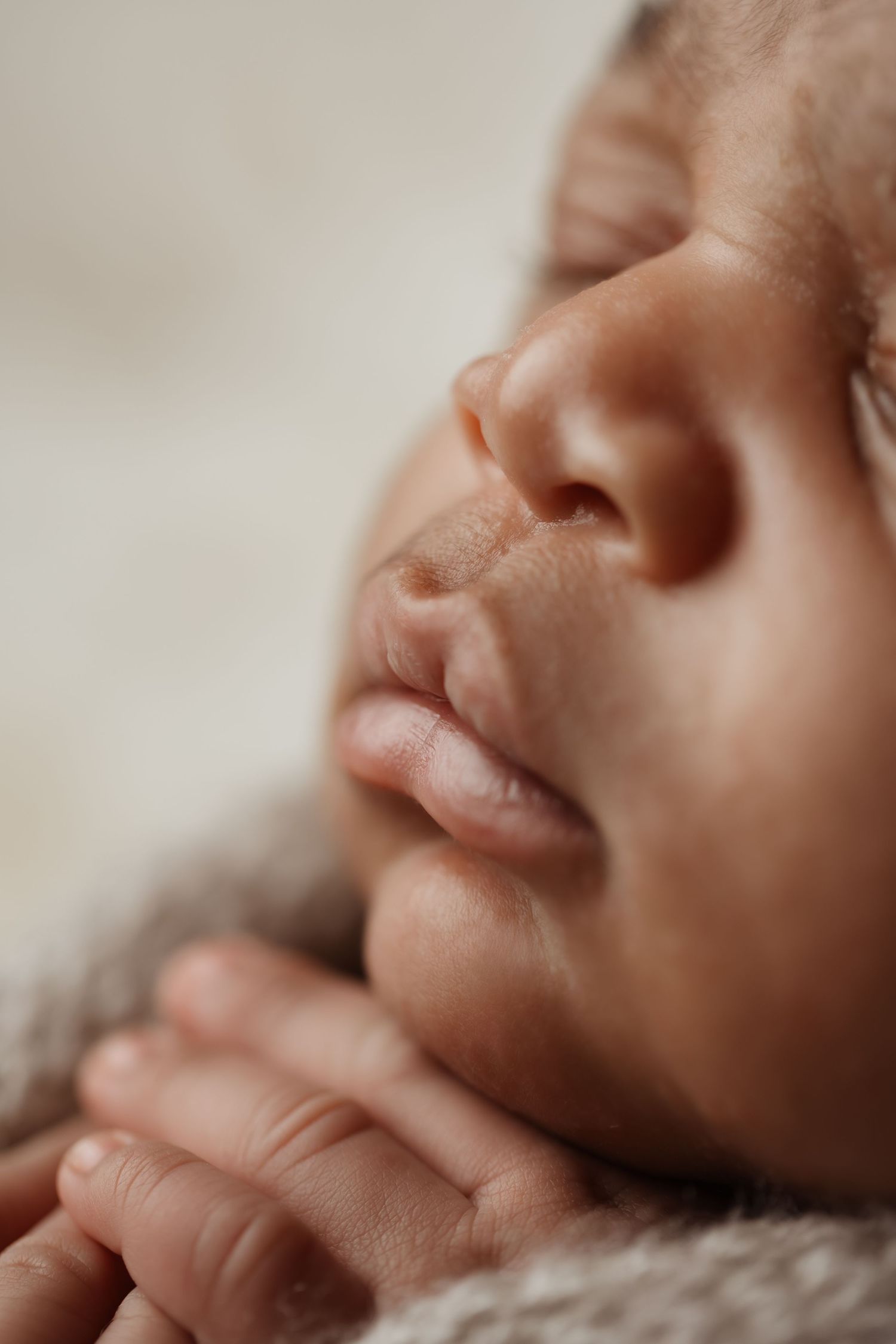 Close-up portrait of a sleeping newborn baby with tiny fingers tucked under chin, peaceful expression.
