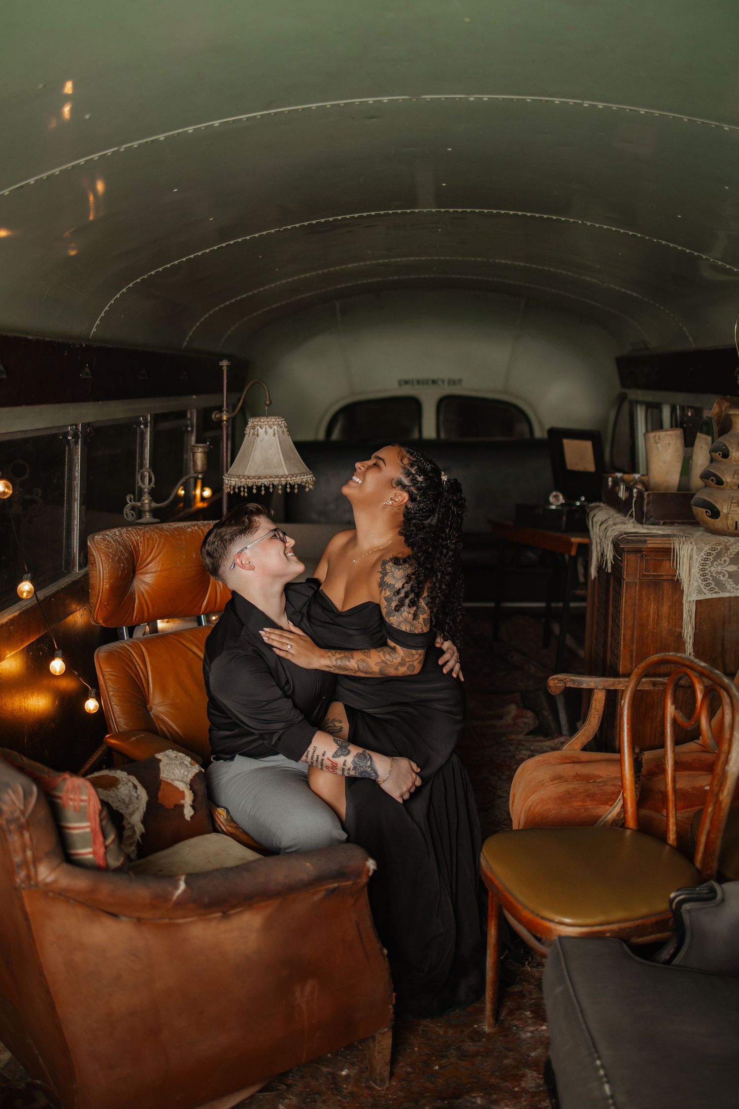 Couple embracing romantically inside a vintage bus converted with antique furniture and warm string lights.