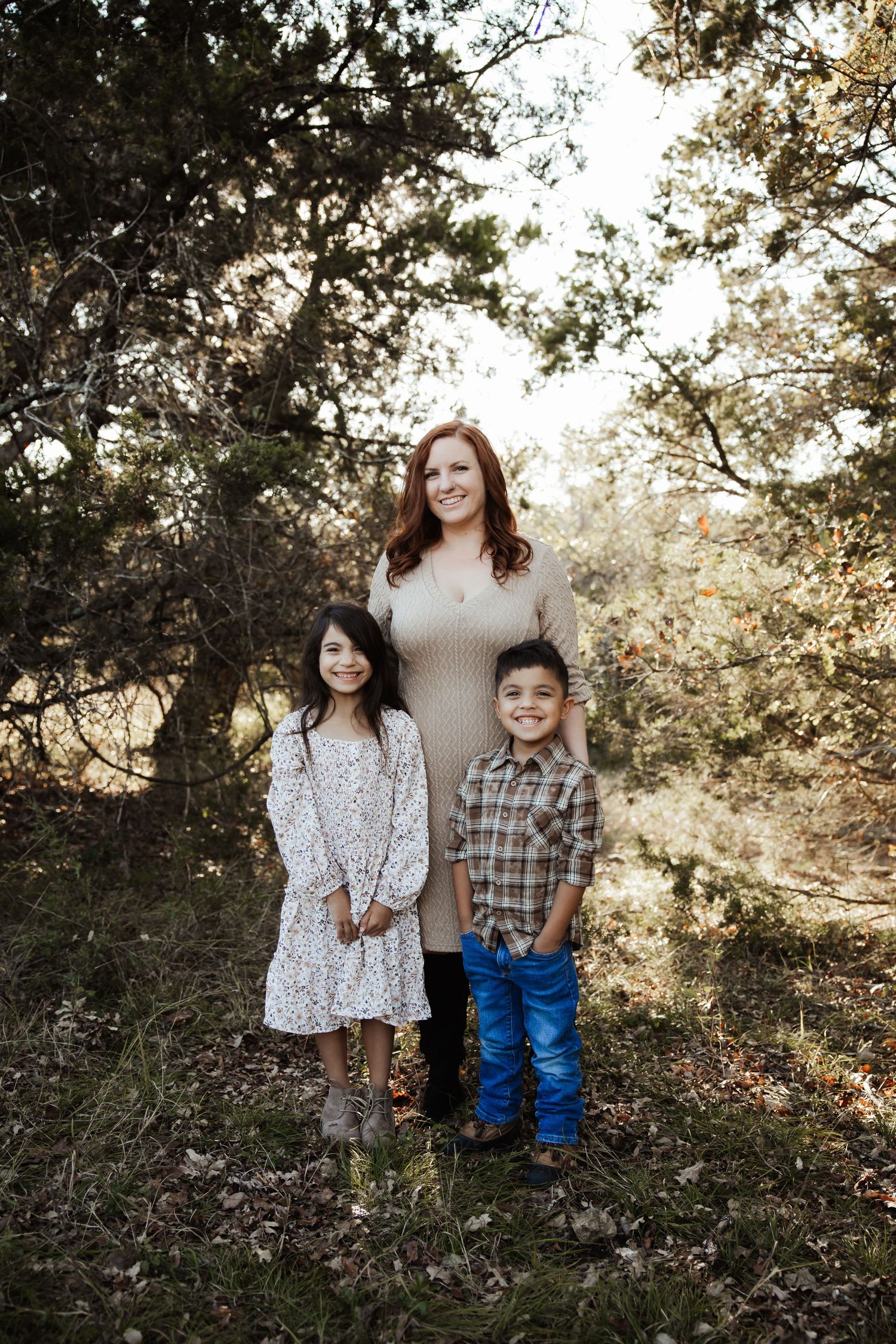 Redhead mother posing with two young children in a wooded outdoor setting.