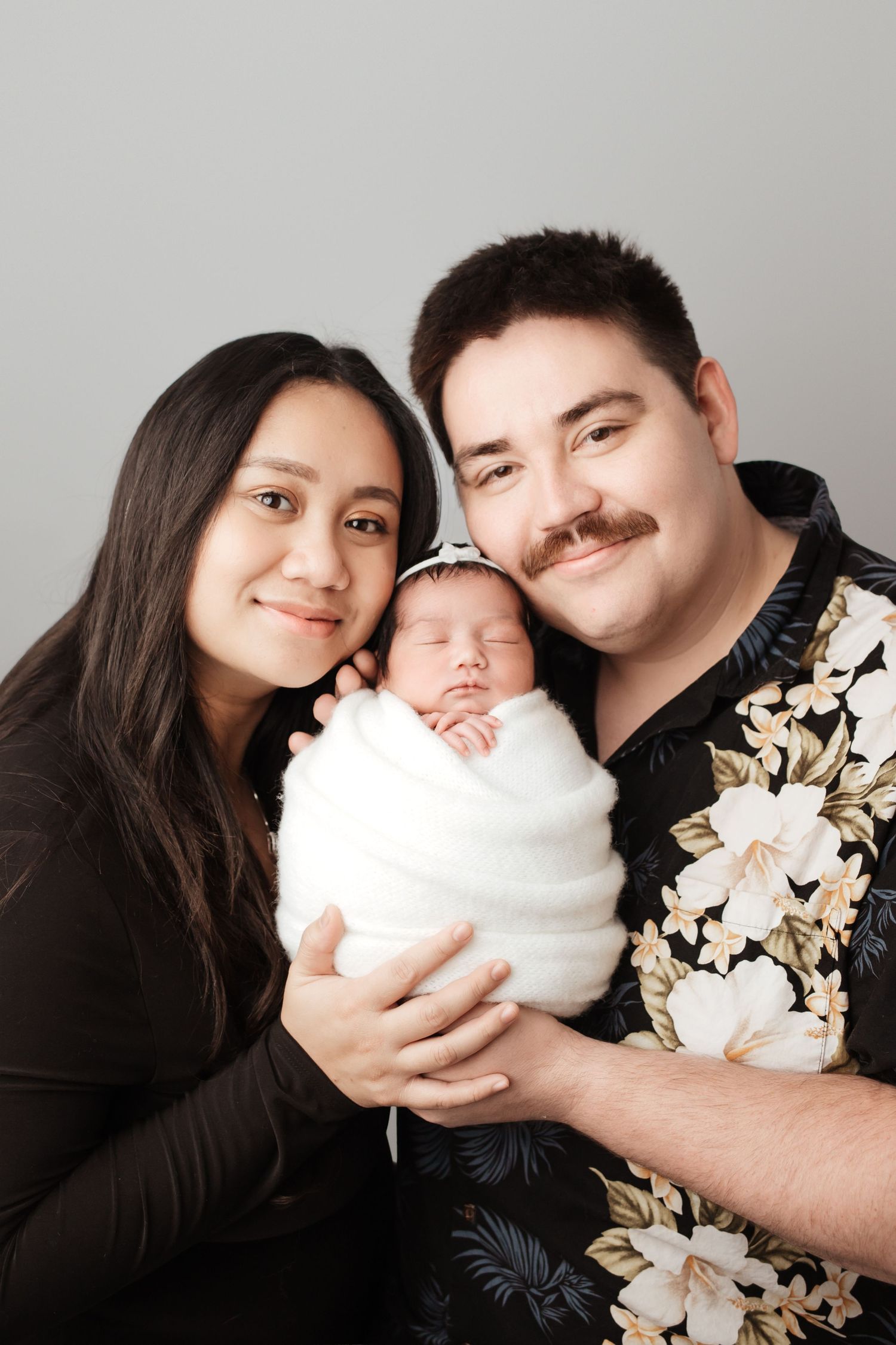 Happy family portrait with parents holding their swaddled newborn baby.
