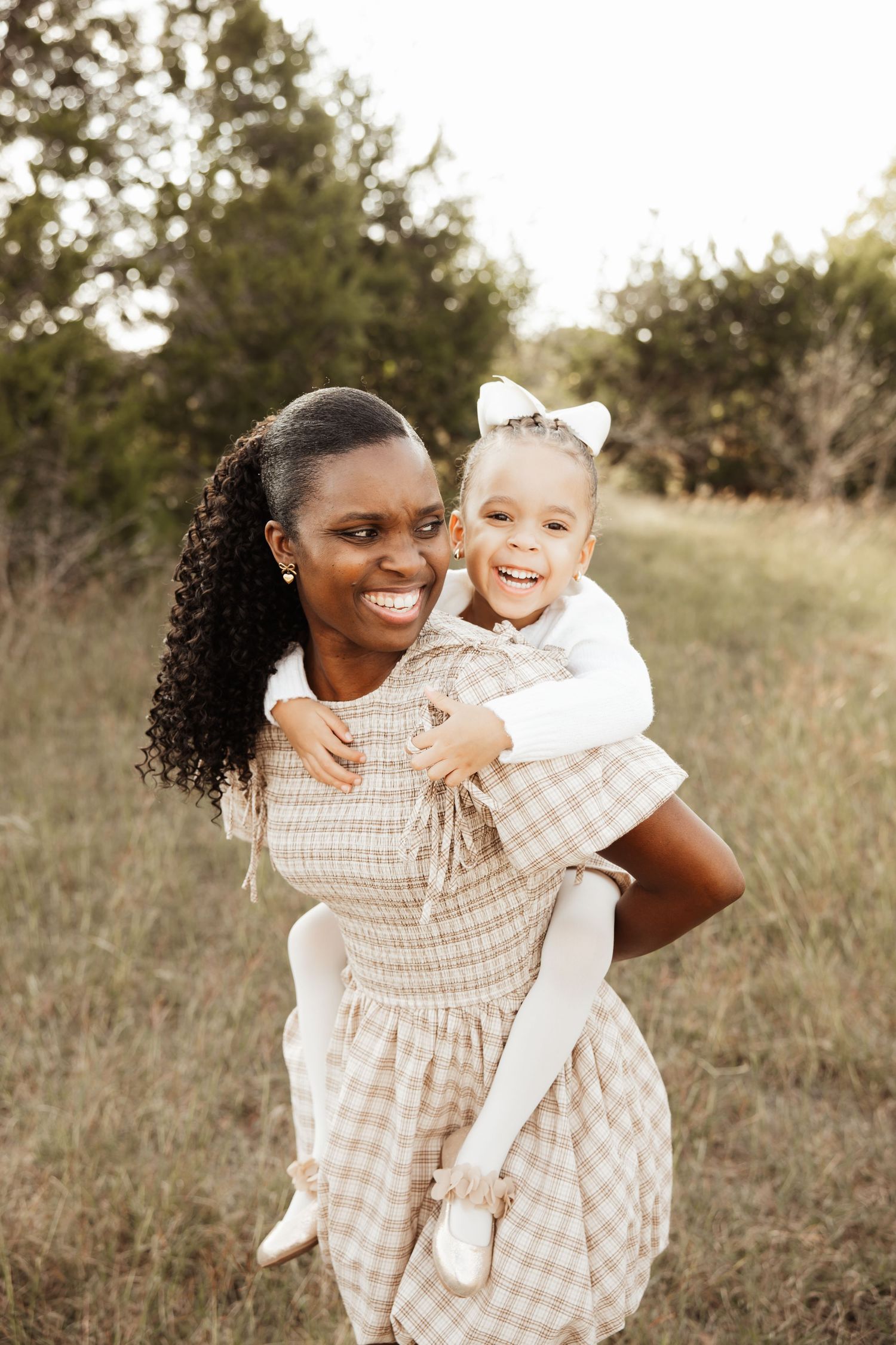 Smiling Black mother giving young daughter a piggyback ride in an outdoor field.