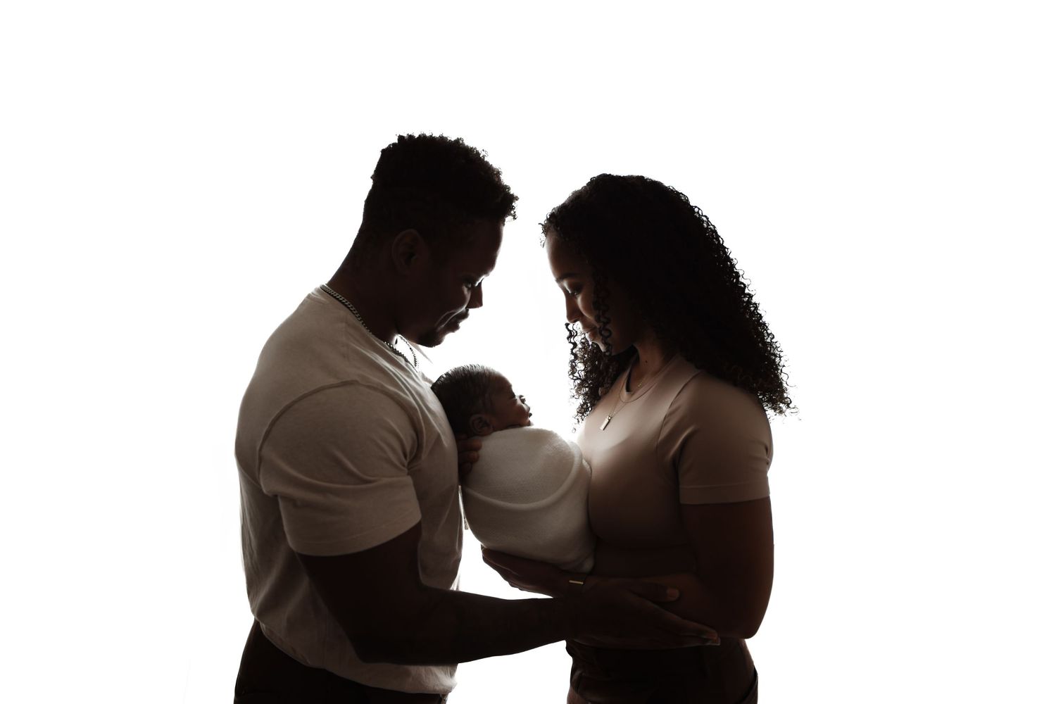Silhouette of a couple lovingly cradling their newborn baby against a bright white background.