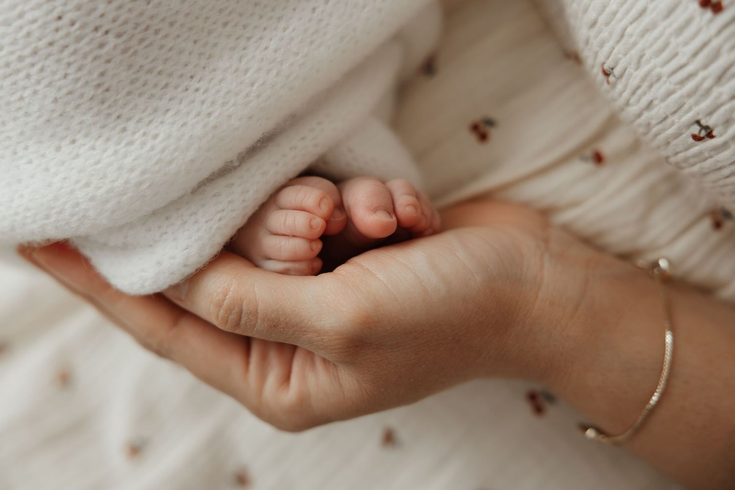 Close-up of newborn baby tiny feet held in mothers hand during lifestyle newborn session.