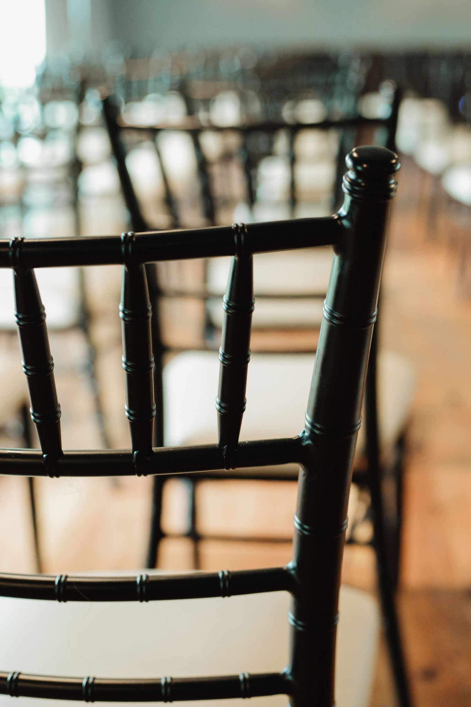 Rows of elegant black Chiavari chairs arranged in a bright event venue for a wedding or formal gathering.