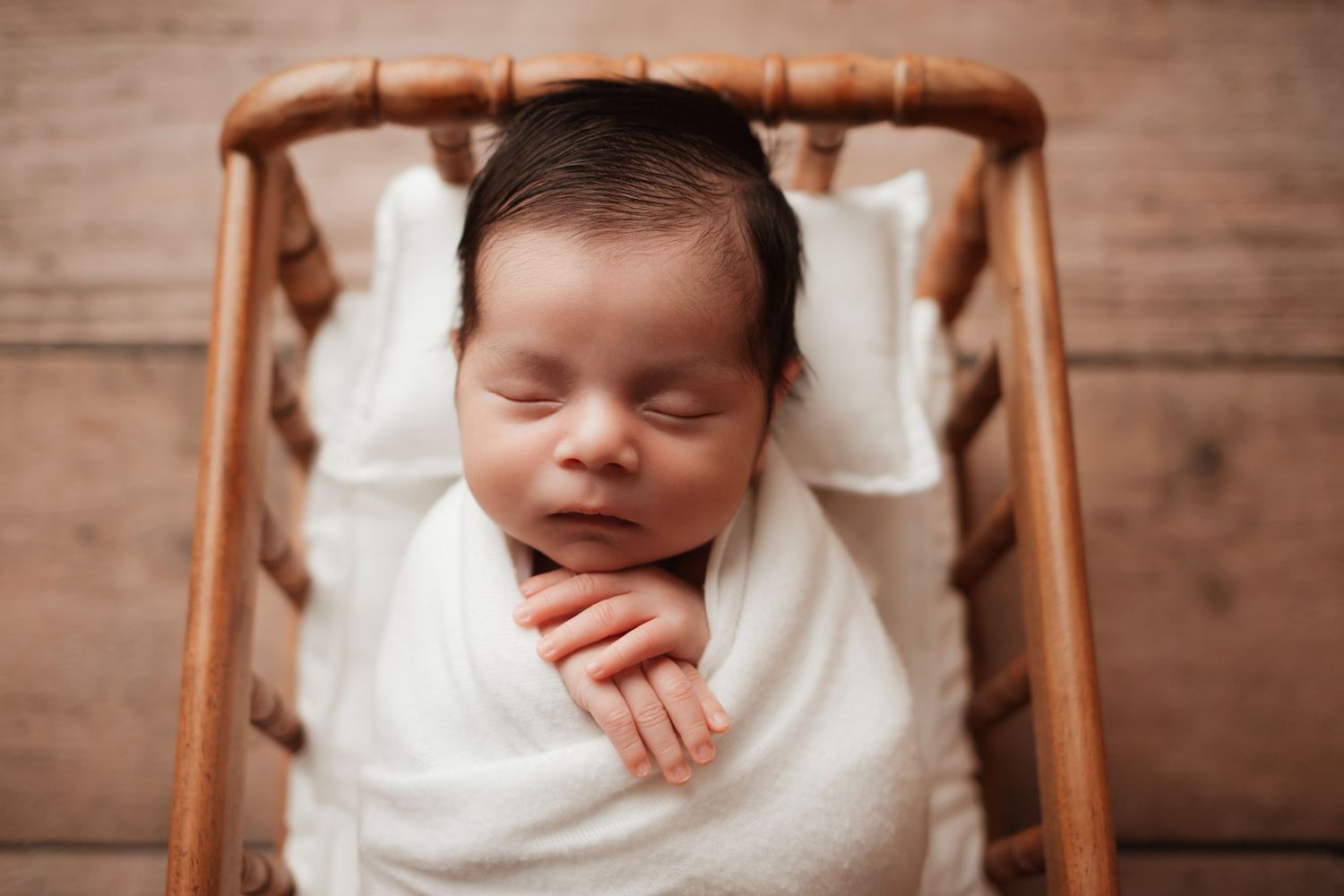 Sleeping newborn baby swaddled in white wrap lying in a small wooden cradle.
