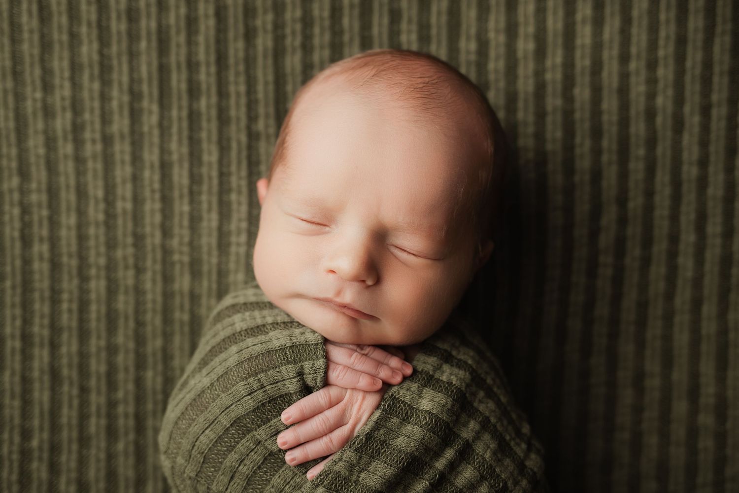 Peaceful sleeping newborn baby swaddled in a green ribbed knit wrap on matching background.