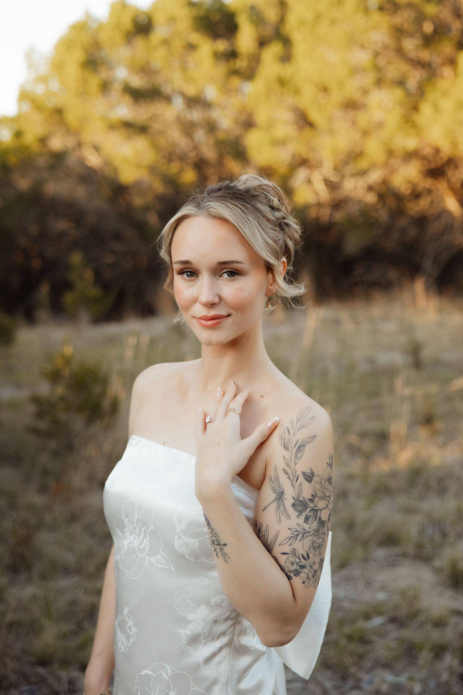 Bride in strapless white gown with floral tattoo poses outdoors at golden hour.