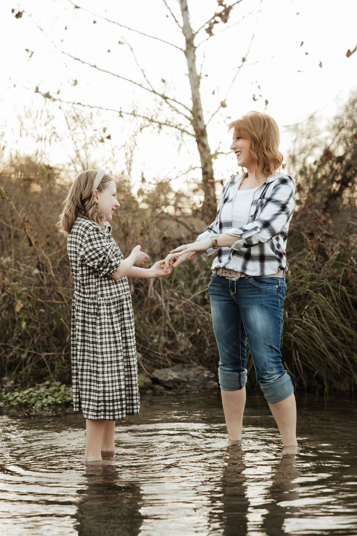 A redheaded mother and daughter in plaid laugh together while standing in a creek.
