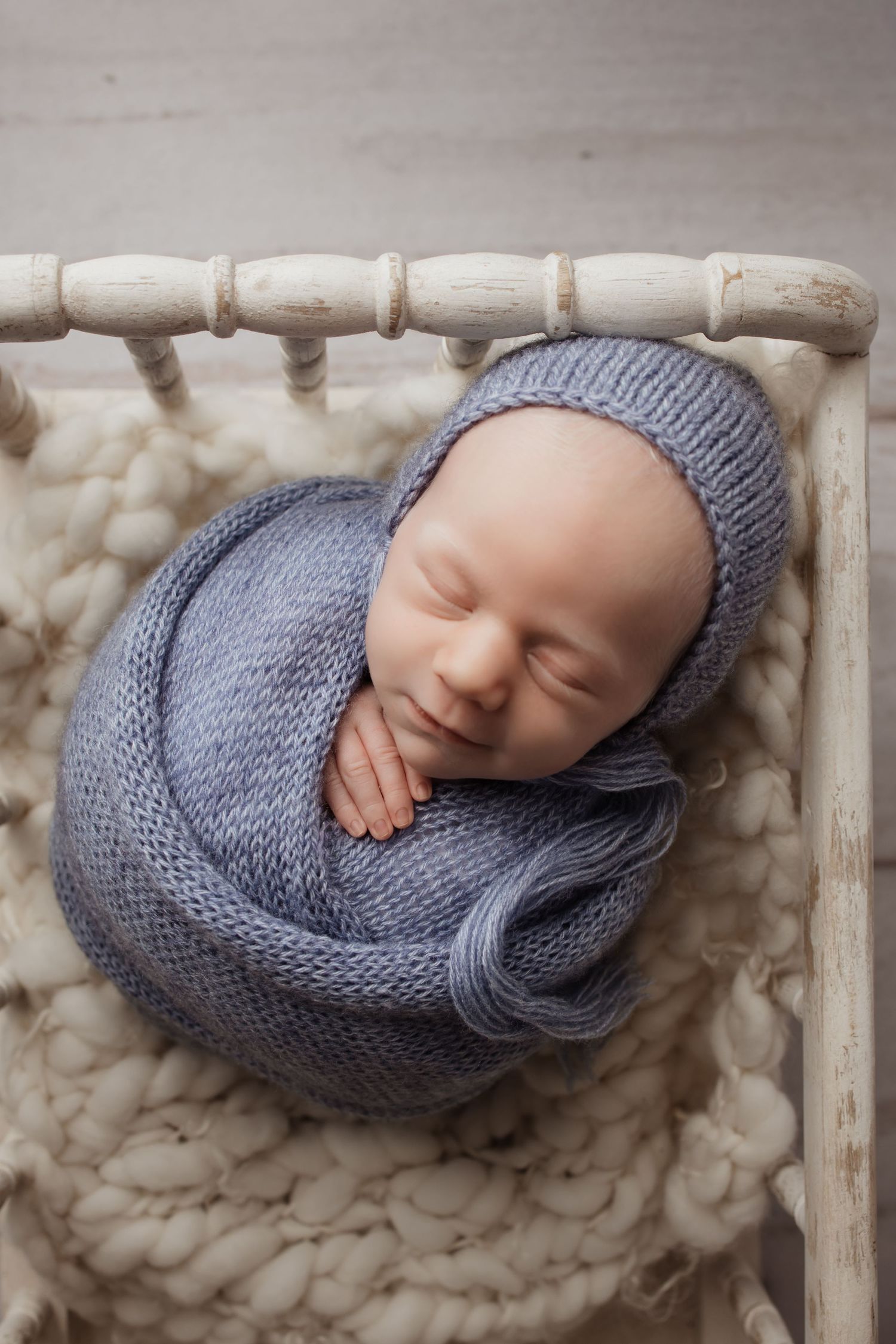 Sleeping newborn baby wrapped in a purple knit swaddle and bonnet in a white wooden crib.
