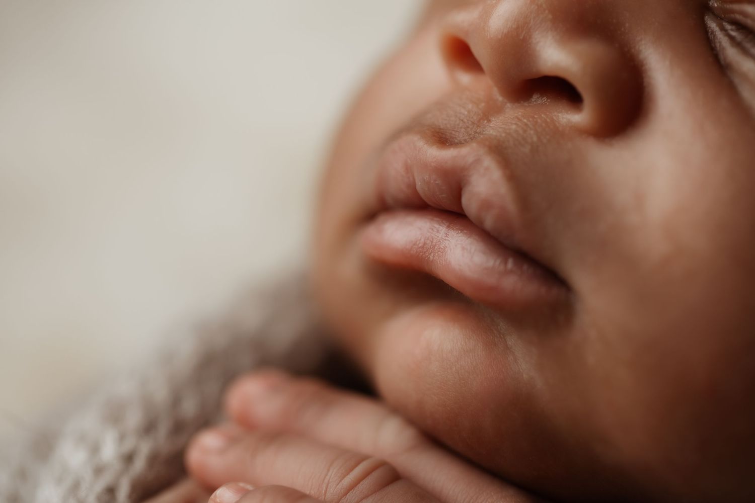 Extreme close-up macro photo of a newborn babys delicate lips and tiny fingers resting on chin.