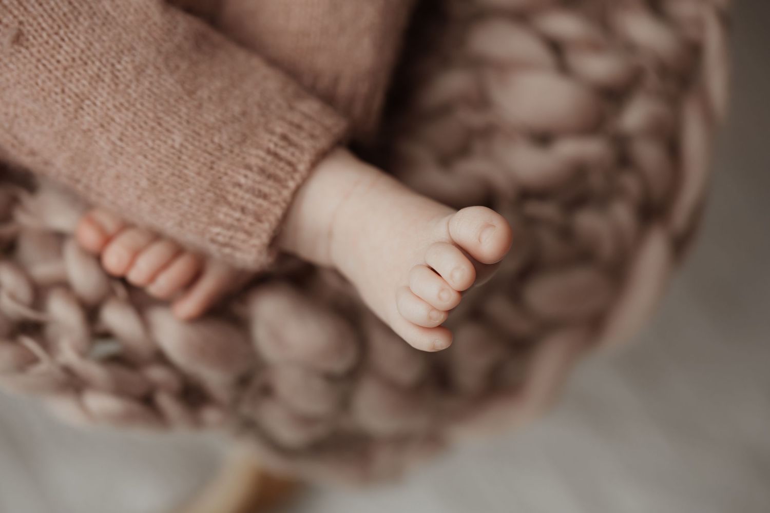 Macro close-up of tiny newborn baby feet and toes resting on a chunky knit pink blanket.