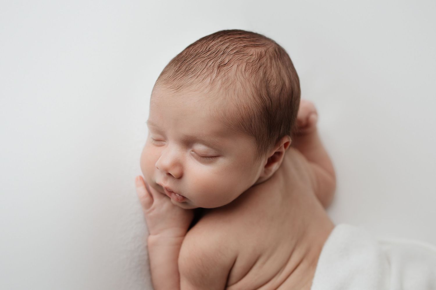 Sleeping newborn baby rests gently in parent's supportive hands in a tender close-up portrait.