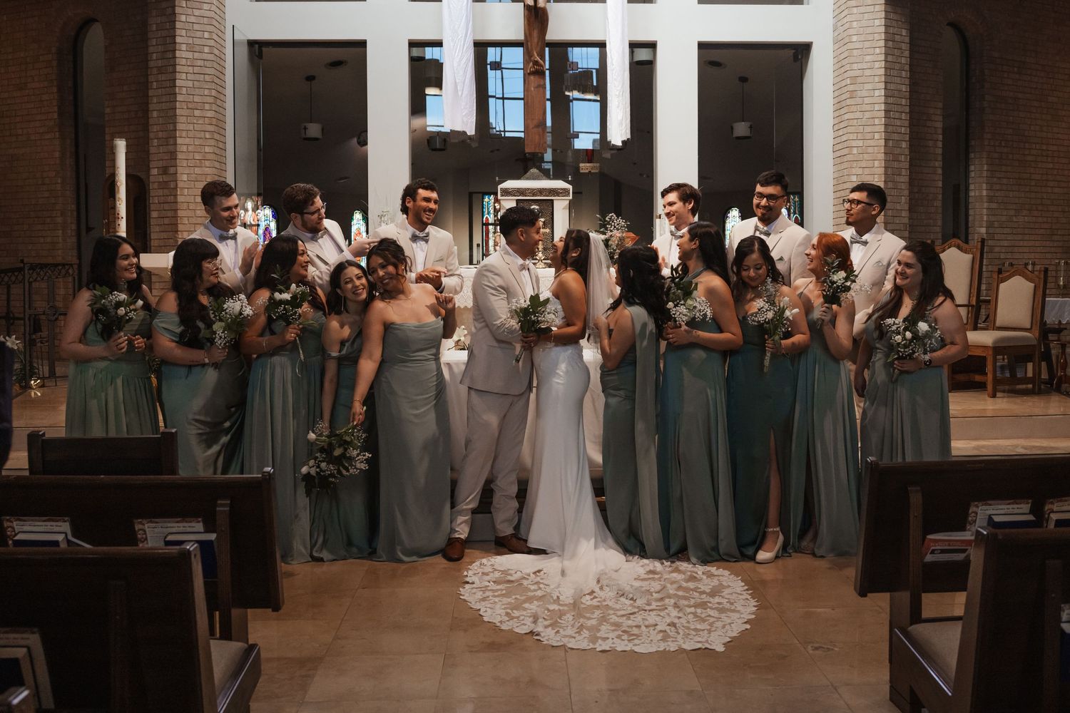 Wedding party poses in a church, bridesmaids in sage green gowns flanking the bride and groom during the ceremony.
