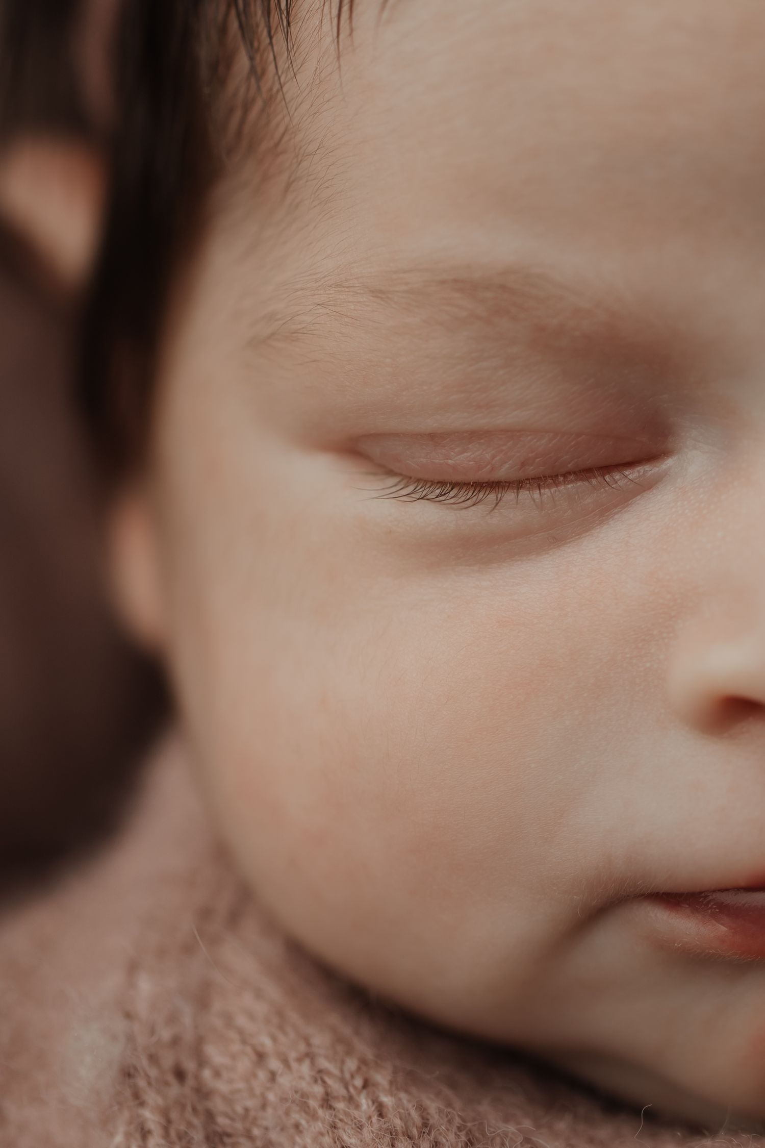 Extreme close-up macro portrait of a peaceful sleeping newborns face showing delicate eyelashes and soft skin.
