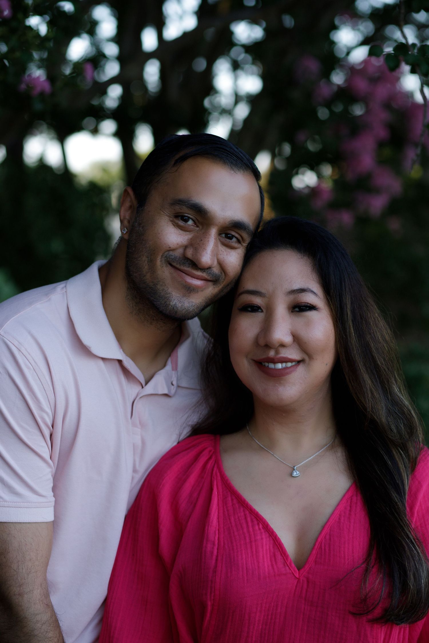 Happy couple smiling together outdoors with blooming pink flowers in the background.