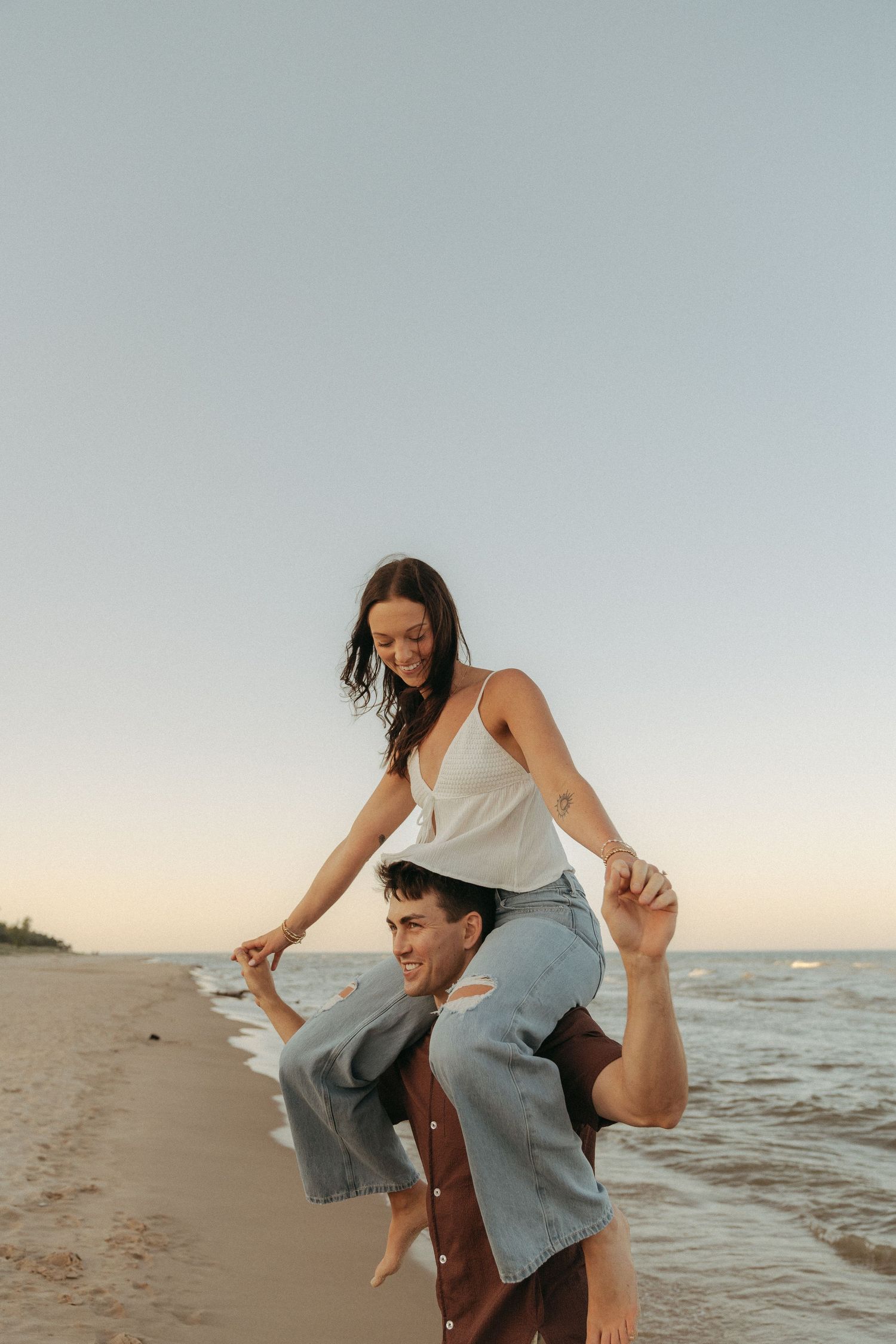 A man carrying a woman on his back while walking on a beach at sunset.