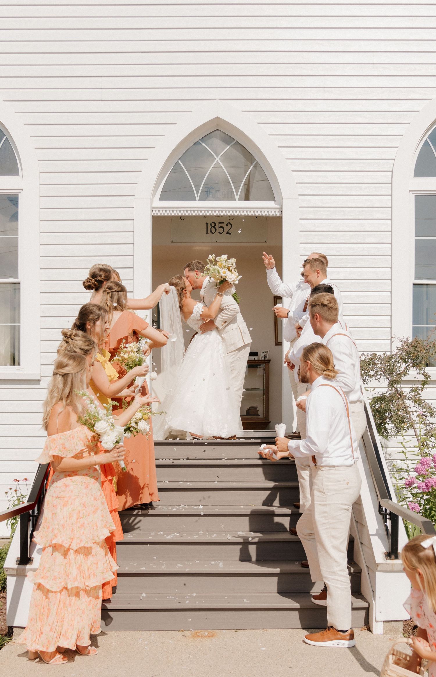 A group of people, including a bride and groom, standing on the steps of a white church building.